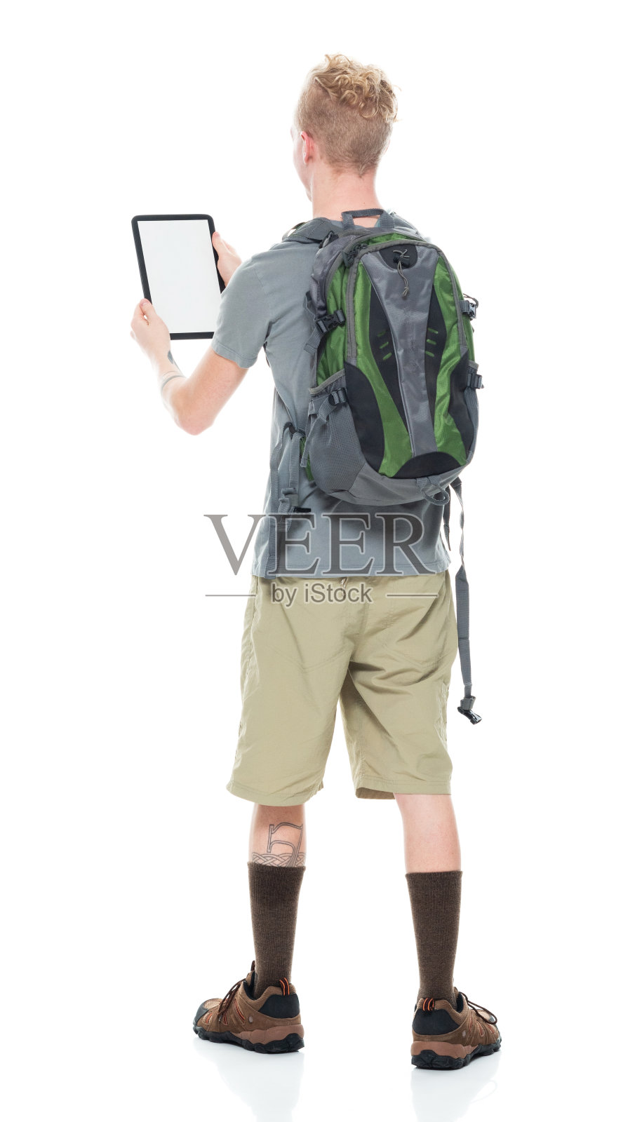 白人年轻男性背包客在白色背景前徒步旅行，穿着短裤，拿着包，使用数码平板电脑照片摄影图片