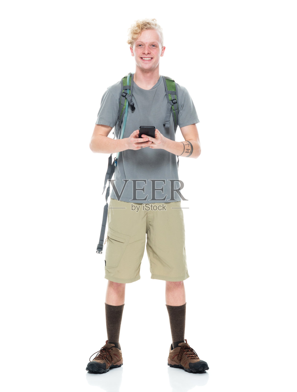 白人男性背包客穿着短裤，拿着包，用手机在白色背景前徒步旅行照片摄影图片