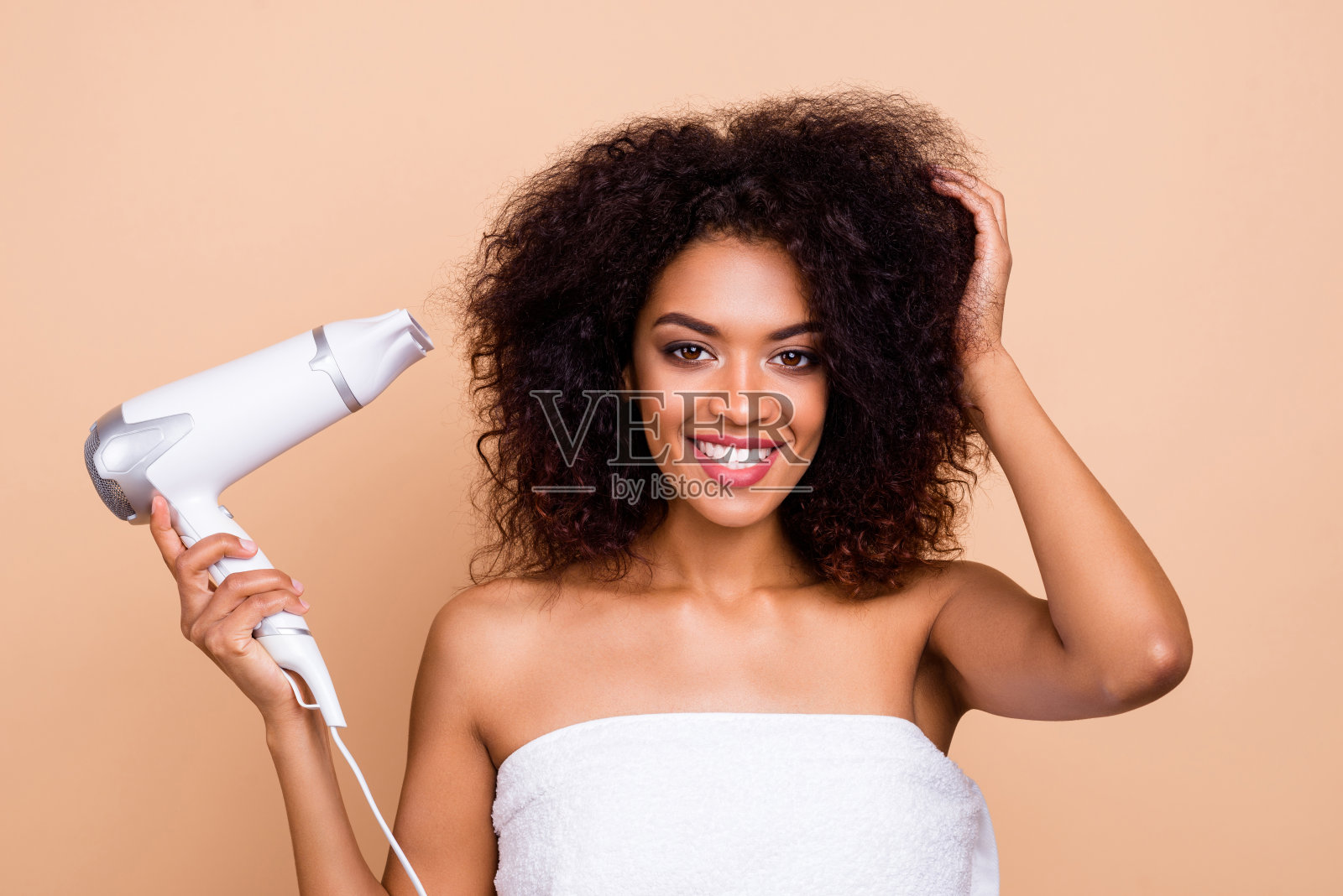 她的近距离肖像，她漂亮迷人，精心打扮，愉快愉快的卷发女孩使用电吹风准备派对孤立的米色柔和的背景照片摄影图片