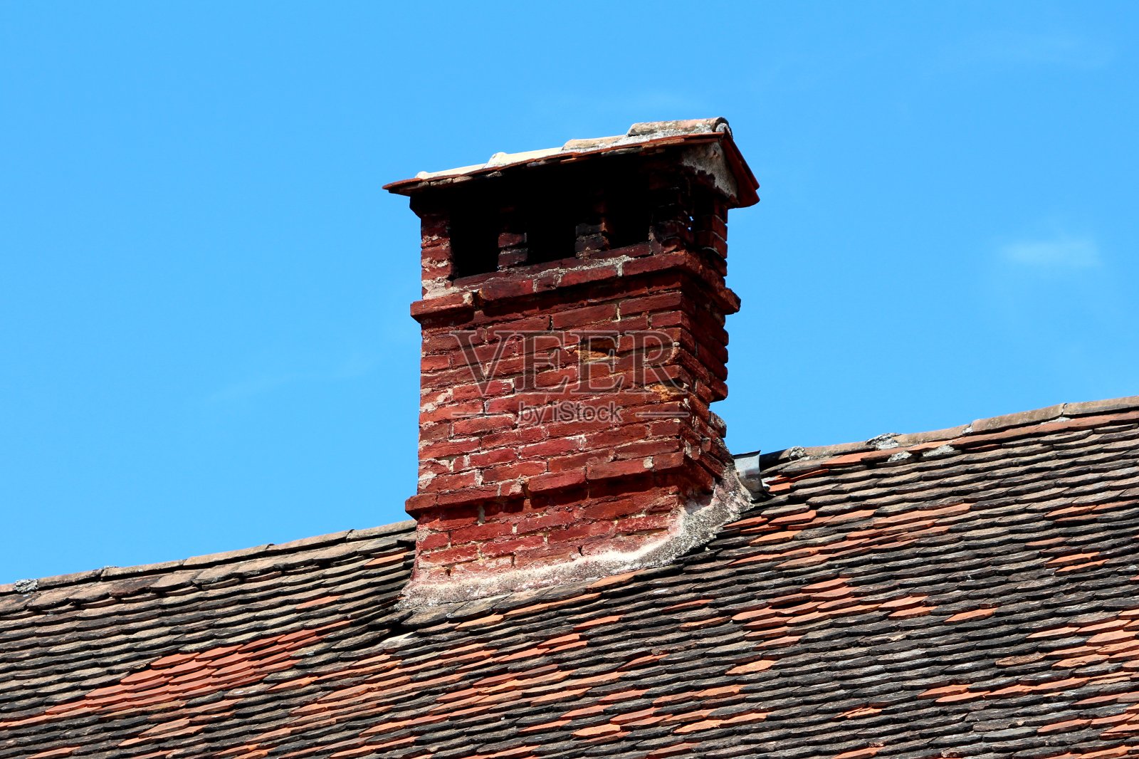 一根细长的、古老的、暗红色的砖把有裂缝的烟囱砸得破破烂烂，烟囱上有多个开口，上面铺着小瓦片照片摄影图片