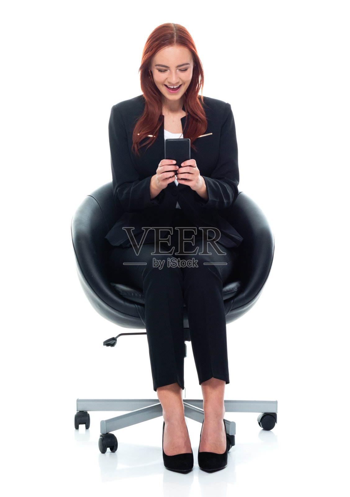 白人年轻女商人坐在白色背景前穿着商务装，使用手机照片摄影图片