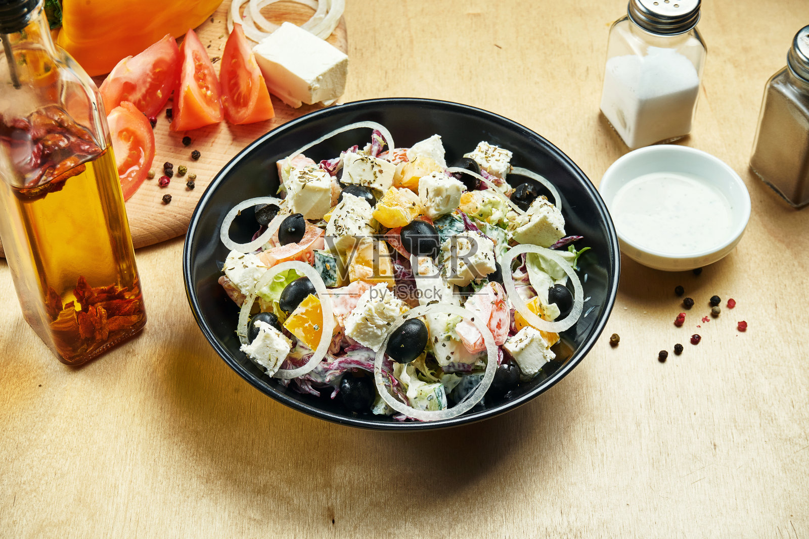 经典的希腊沙拉，用西红柿，洋葱，黄瓜，羊乳酪和黑橄榄放在黑色的碗里，木质的背景。关闭视图。食物平躺照片摄影图片