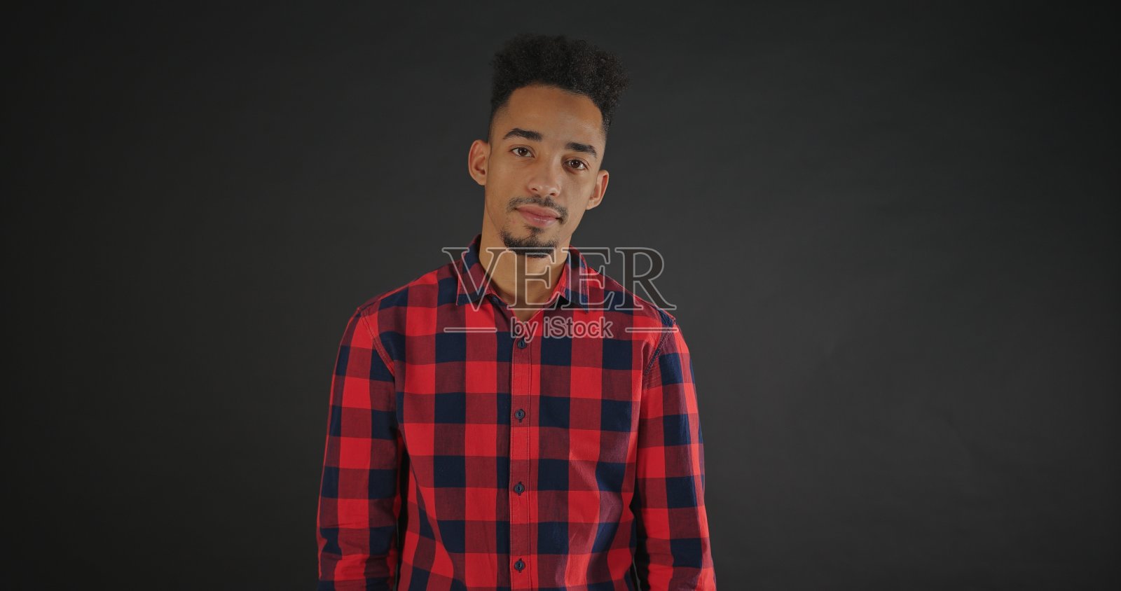 平静的非洲男人穿着衬衫站在黑暗的背景中，看着镜头照片摄影图片