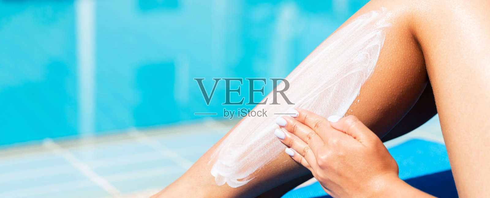 在游泳池边往晒黑的腿上涂防晒霜的女人，度假防晒理念照片摄影图片