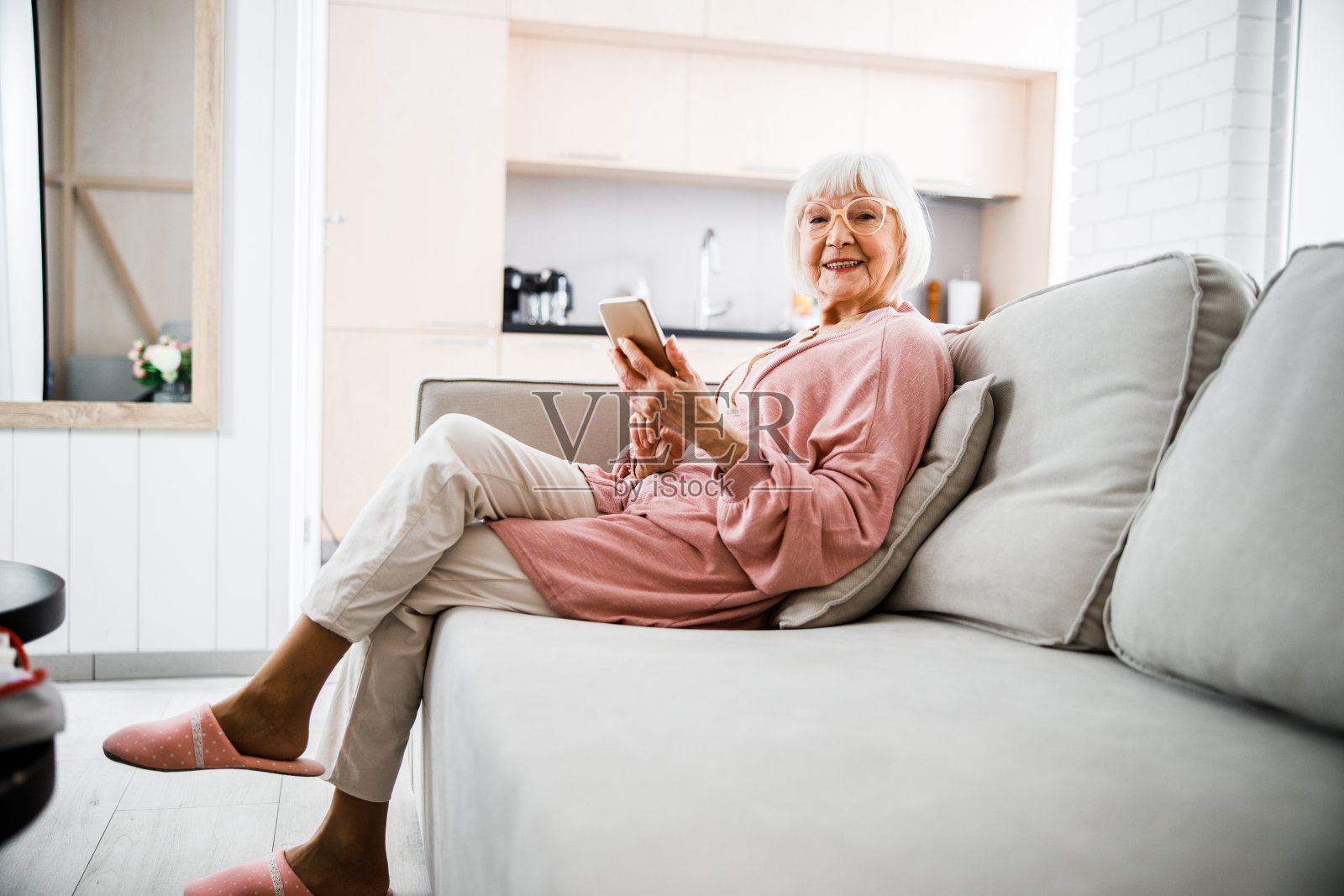 微笑的老妇人坐在沙发上，拿着智能手机照片摄影图片
