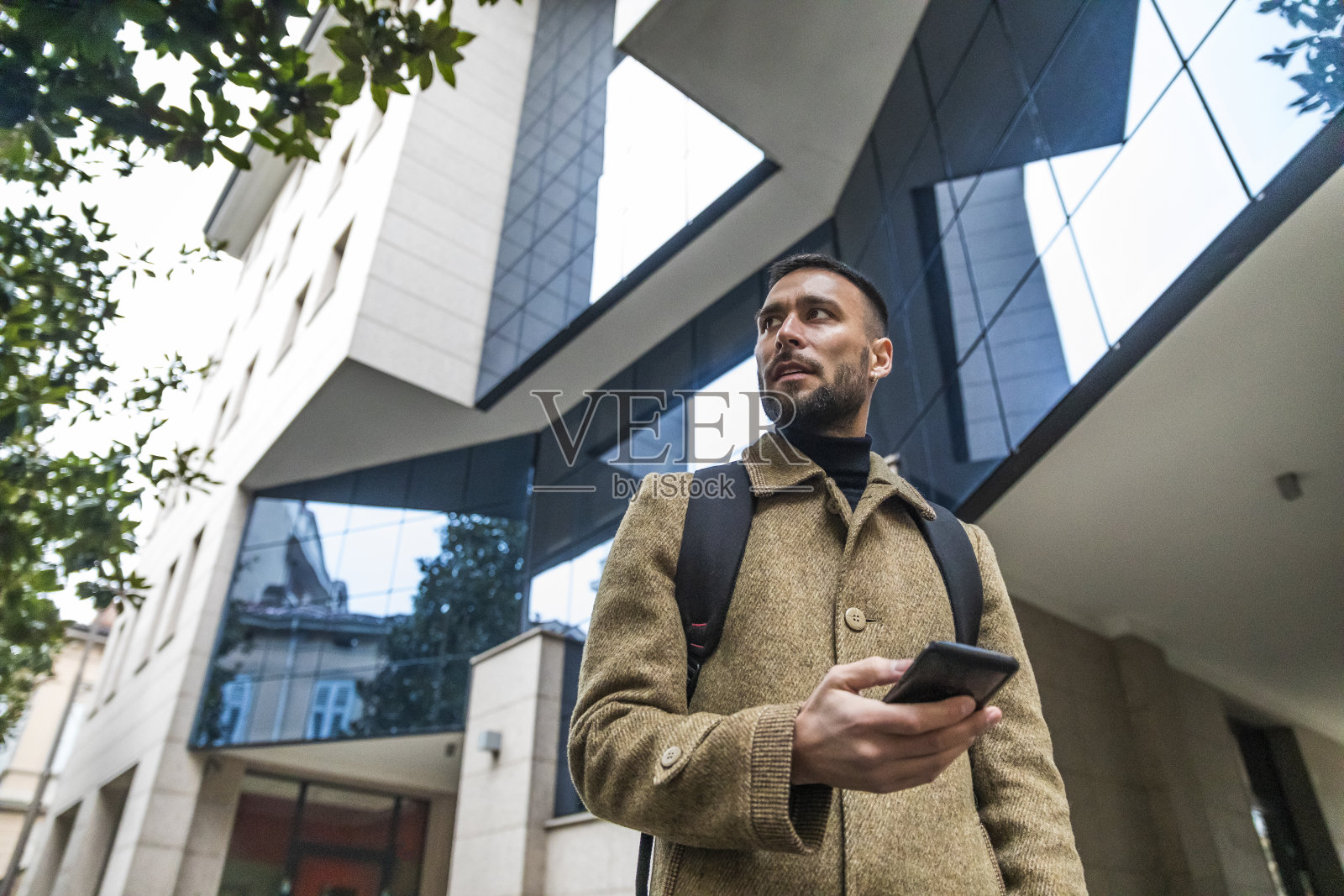 穿着优雅外套，在现代建筑前拿着手机的迷人游客照片摄影图片