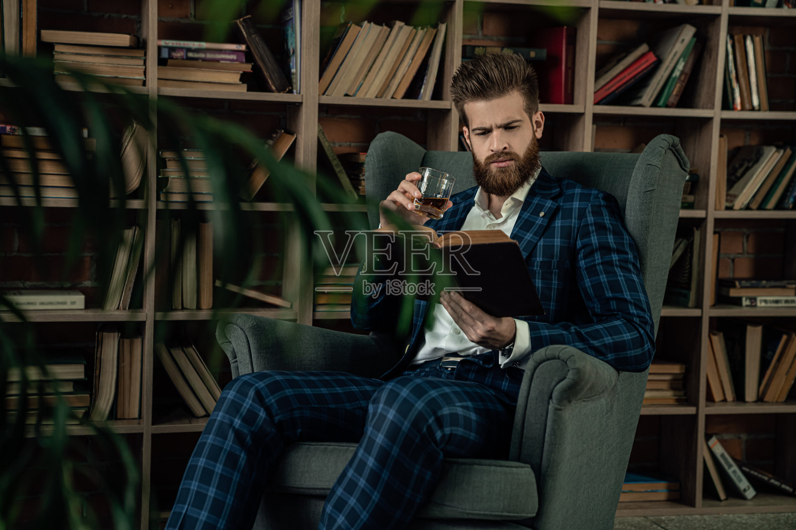 穿着西装，在复古房间里拿着饮料读书的优雅男士照片摄影图片