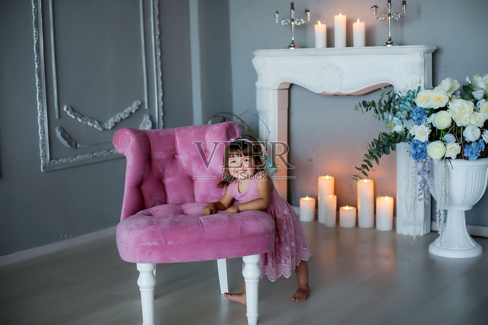 一位年轻的女士在一间点着蜡烛的房间里，正坐在一张粉红色的软垫椅子上开心地笑着照片摄影图片
