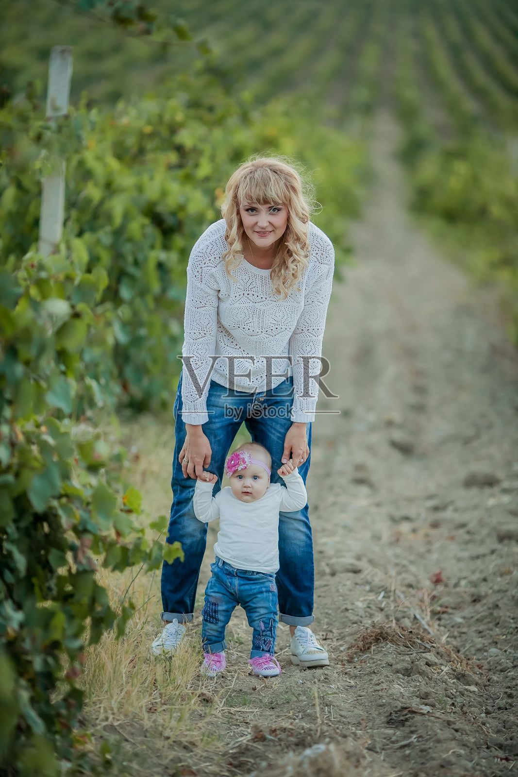 快乐的女人妈妈抱着孩子在一排排的葡萄地里玩耍照片摄影图片