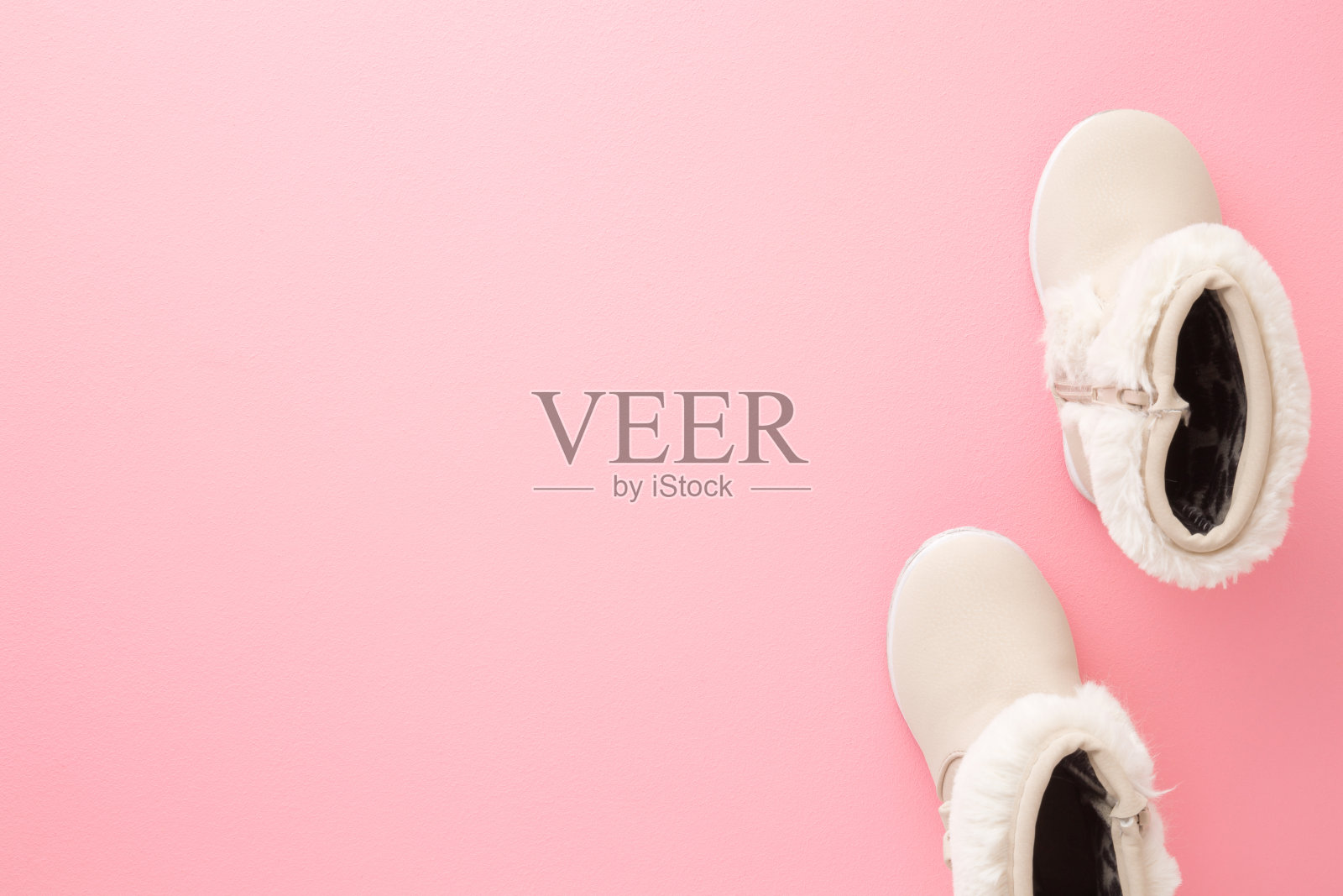 米色皮革温暖婴儿靴子毛绒边浅粉色地板背景。柔和的颜色。文本的空位置。特写镜头。自顶向下的观点。照片摄影图片