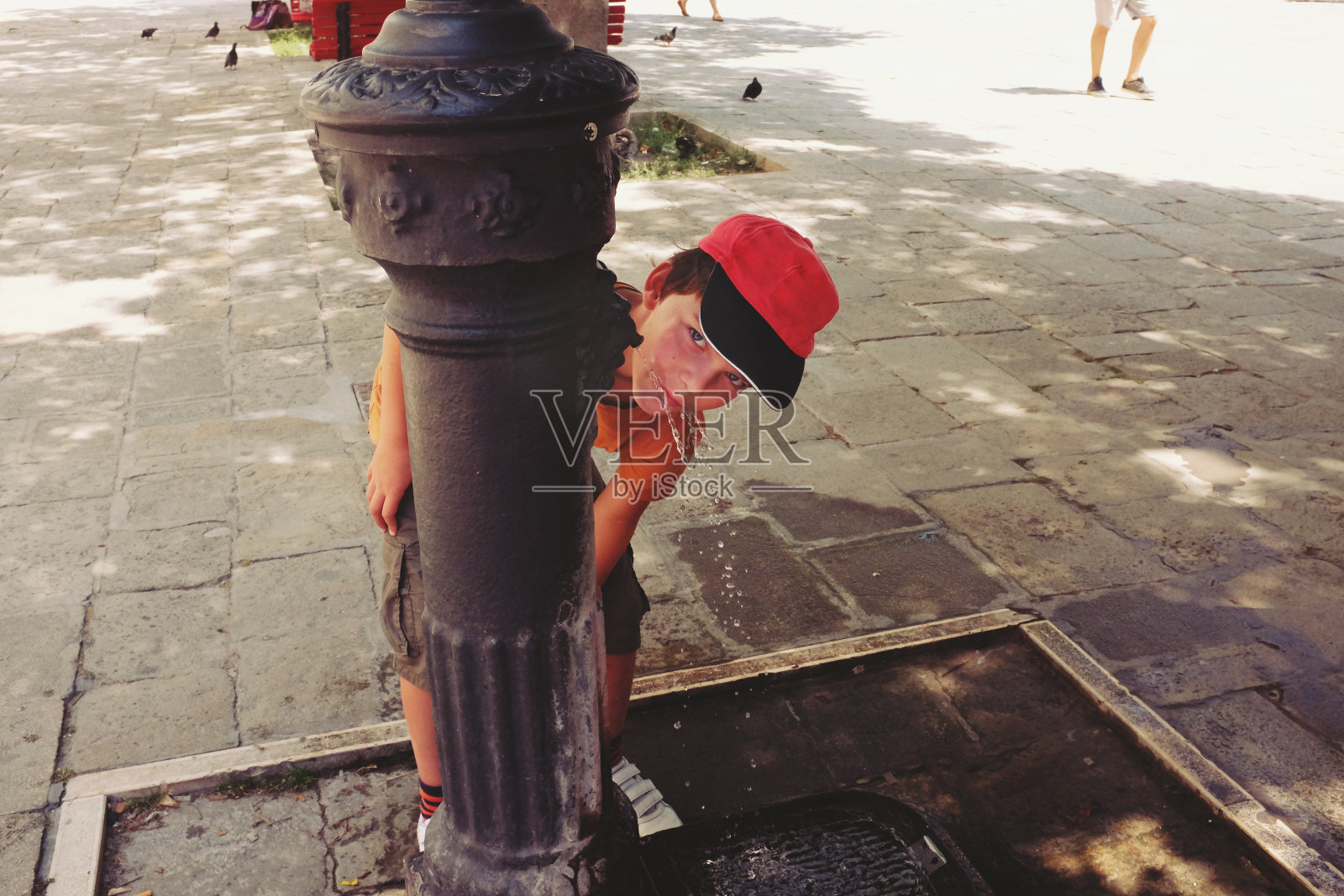在一个炎热的夏天，美丽的淘气男孩在威尼斯广场的饮水机里喝水照片摄影图片
