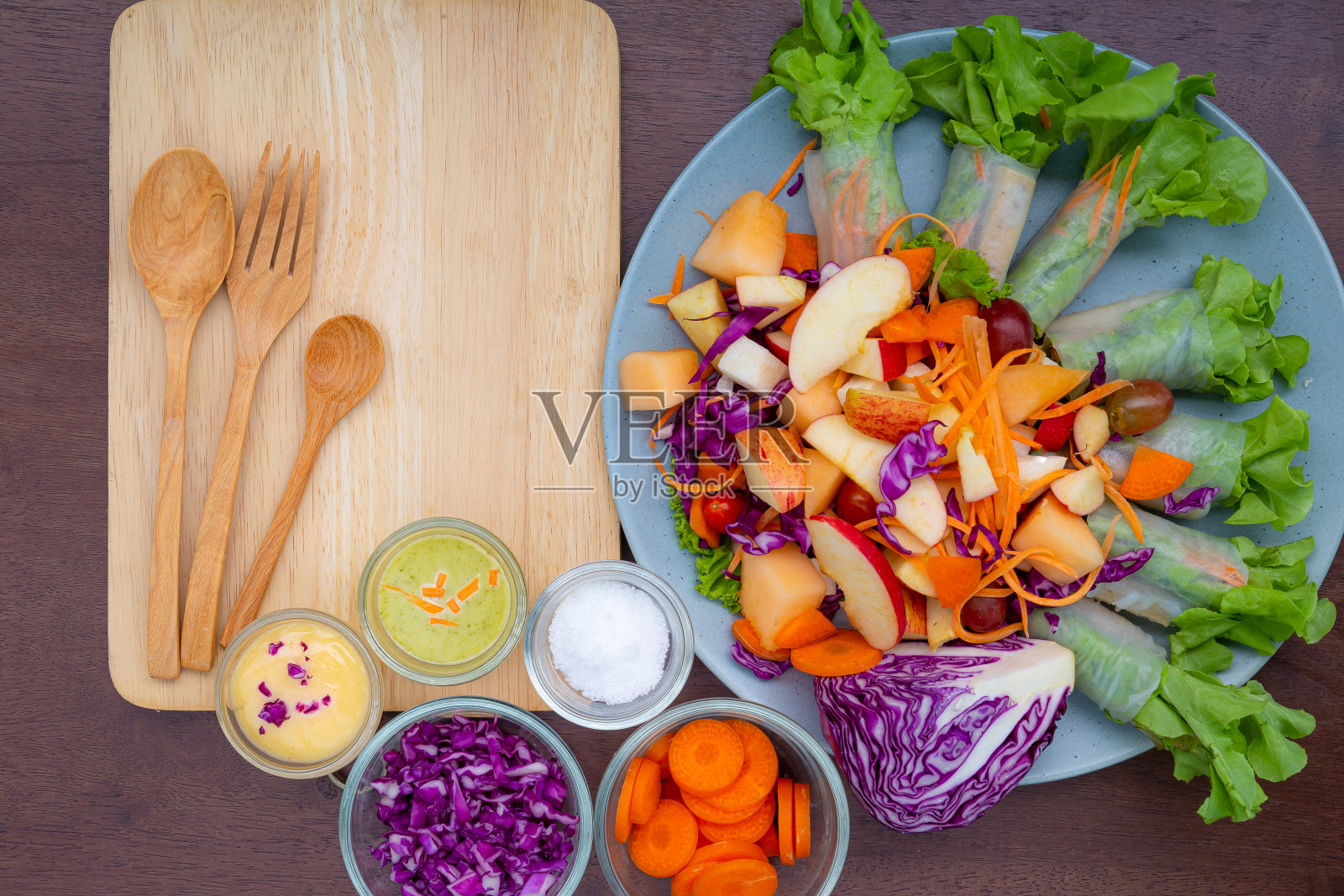 美味的水果沙拉装在一个粘土棕色的盘子里，放在一个切菜板上，有两个甜点叉，薄荷叶，放在一张旧木桌上，特写，俯视图照片摄影图片