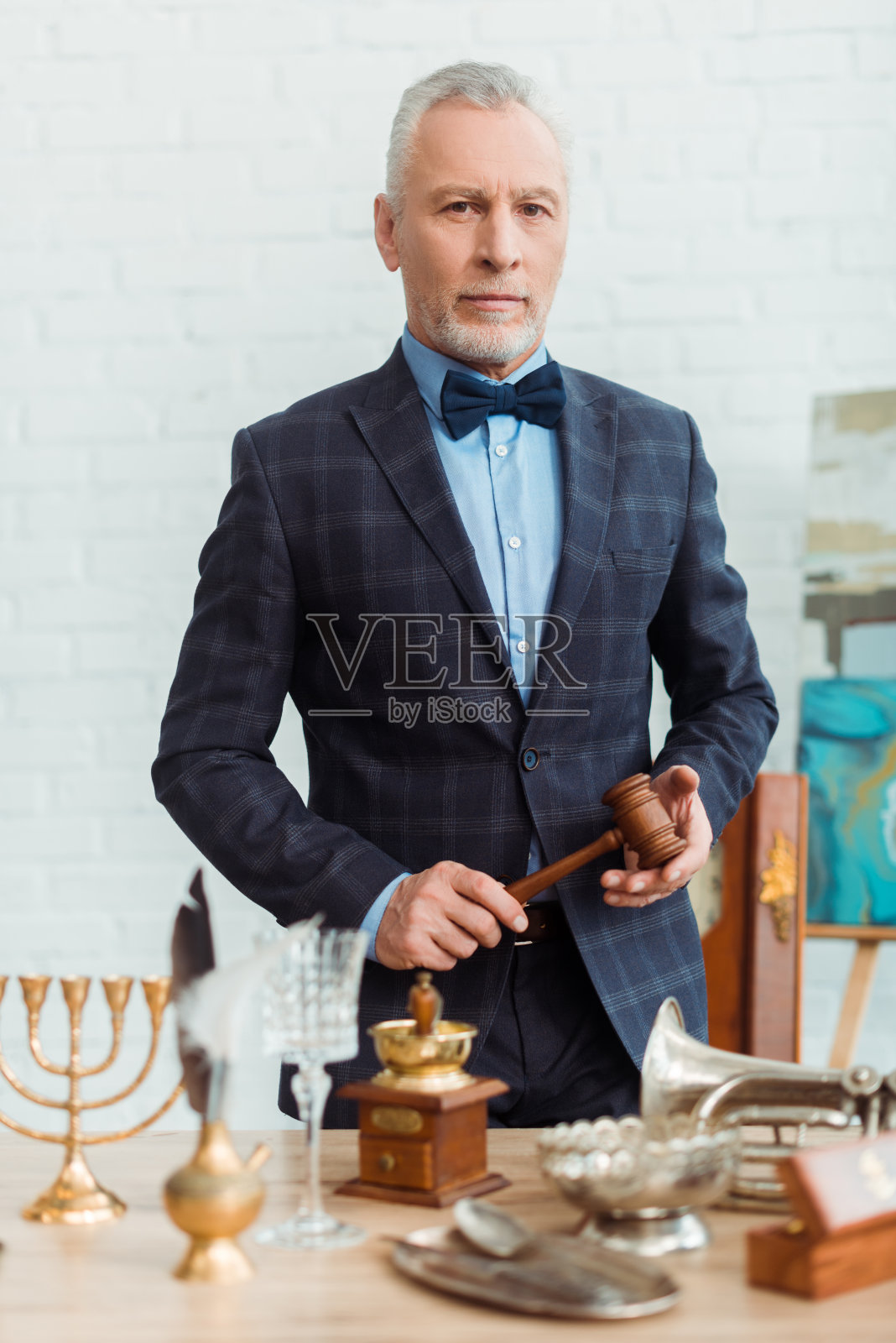 英俊的拍卖师在西装拿着木槌和看在拍卖期间的相机照片摄影图片