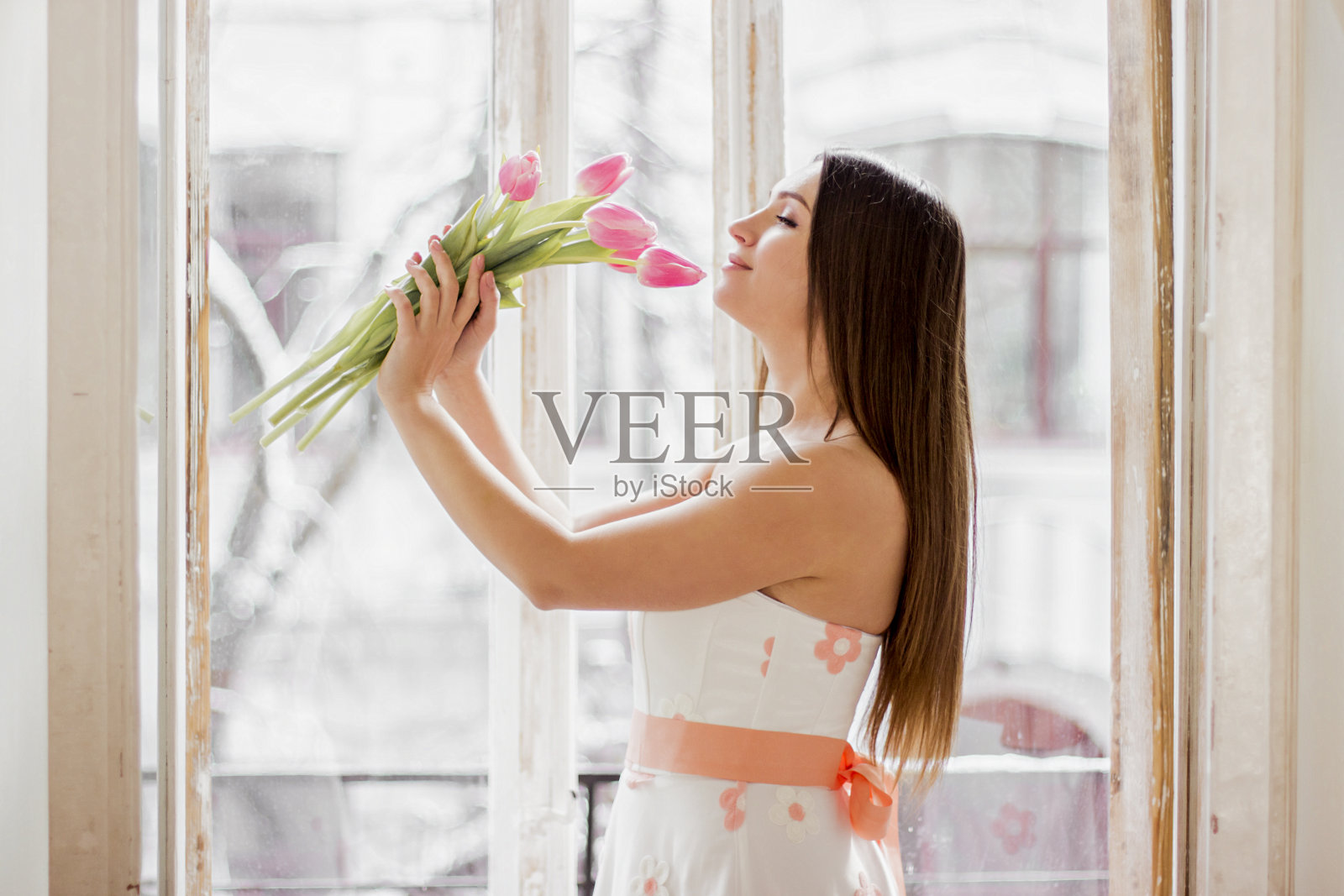 年轻女人穿着漂亮的衣服，闻着花香，面带微笑照片摄影图片