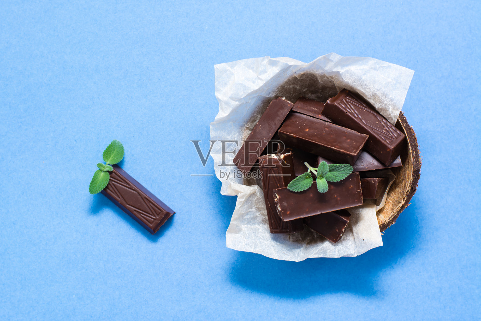 巧克力片和薄荷叶在一个碗和蓝色的纸背景。来自甜食的超重概念。俯视图照片摄影图片