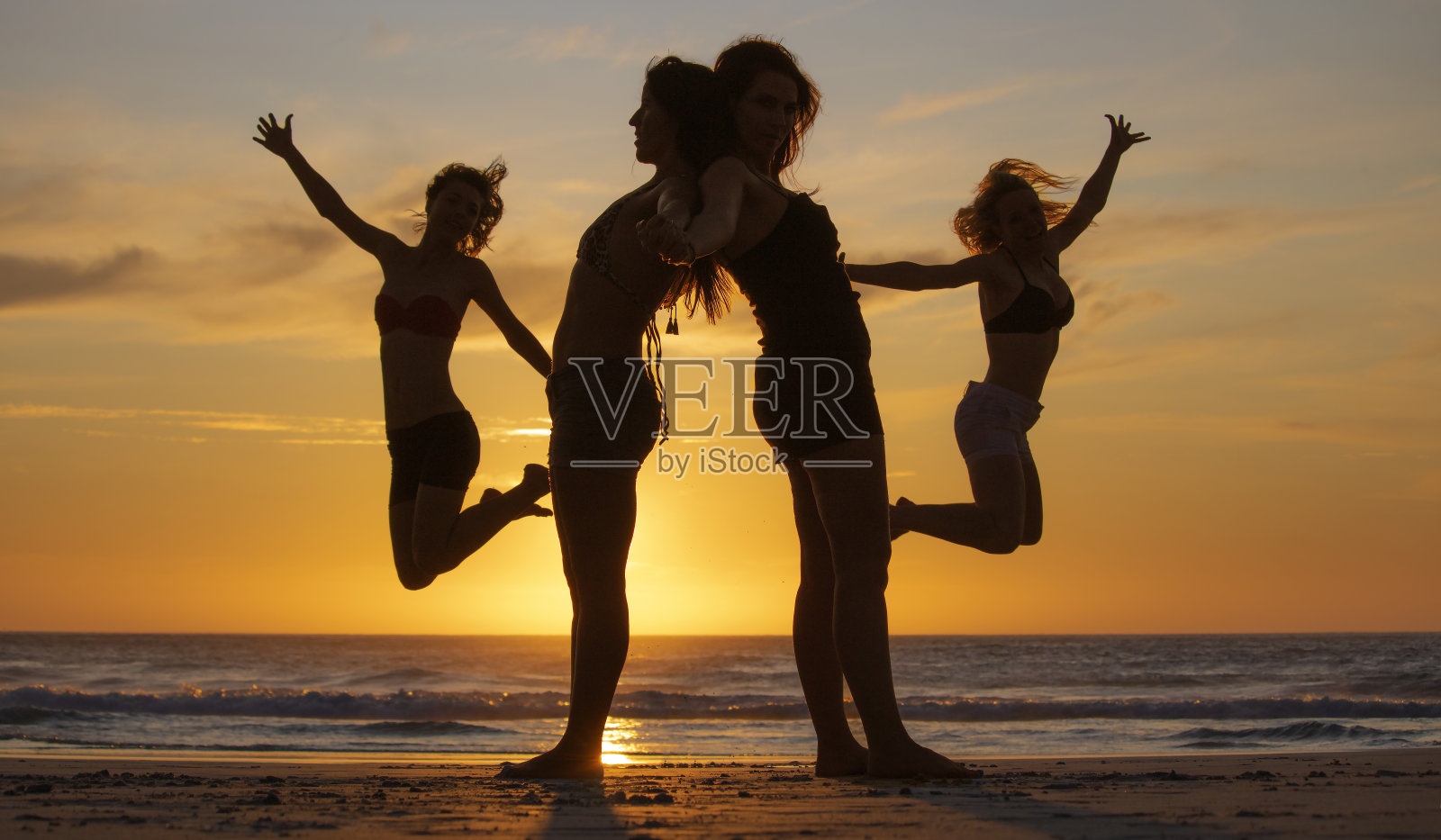 四个美丽女人在海滩日落或日出时创造形状的剪影照片摄影图片