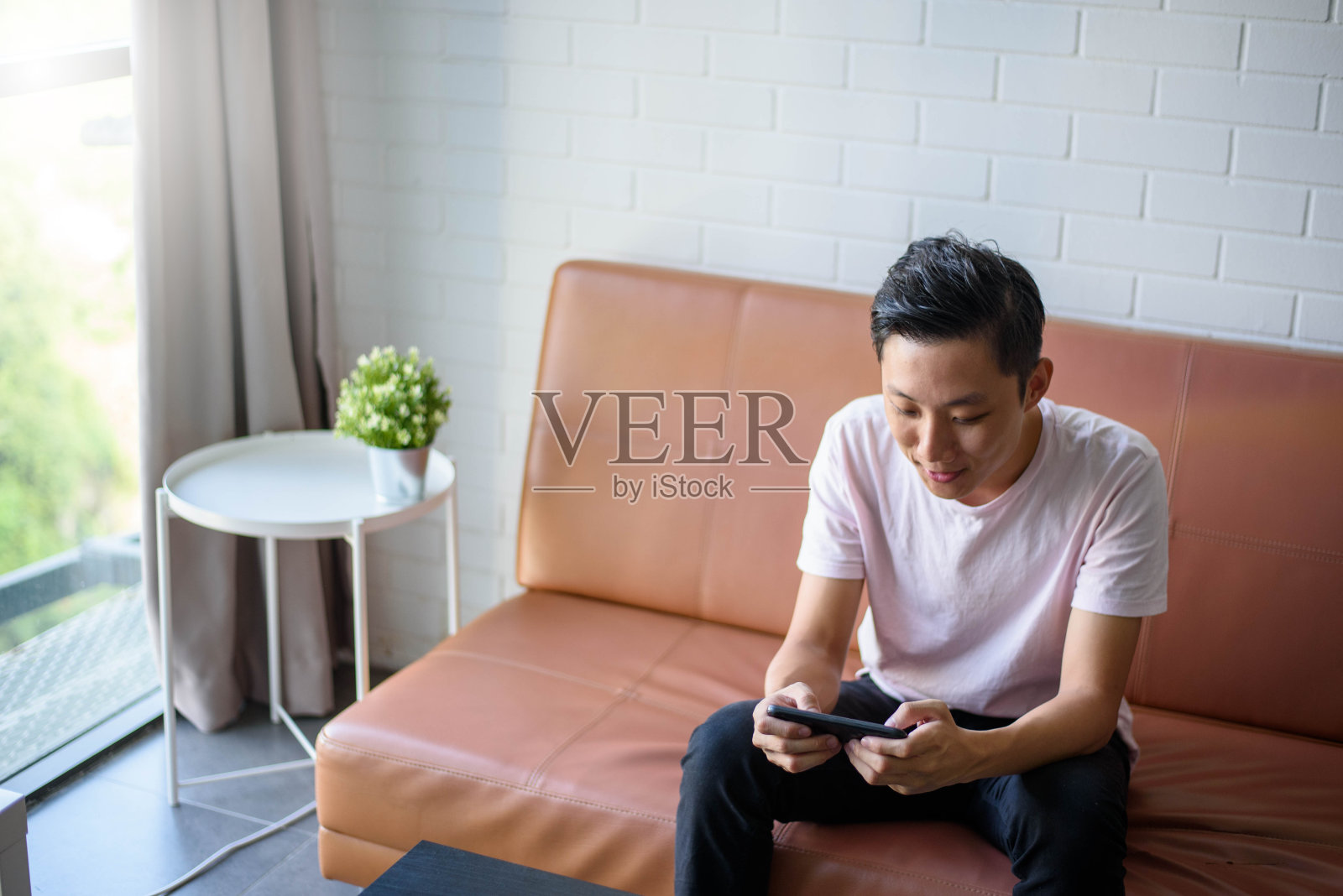 年轻的亚洲男子在客厅用智能手机玩网络游戏照片摄影图片