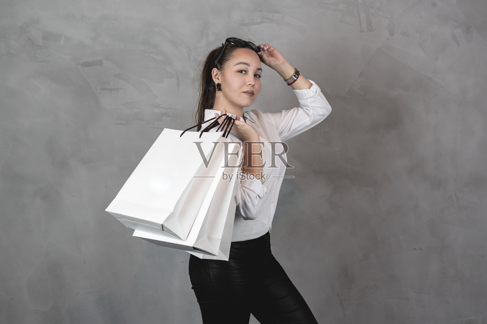 美丽的年轻女子在白色的衬衫和太阳眼镜拿购物袋在灰色的背景应付空间照片摄影图片