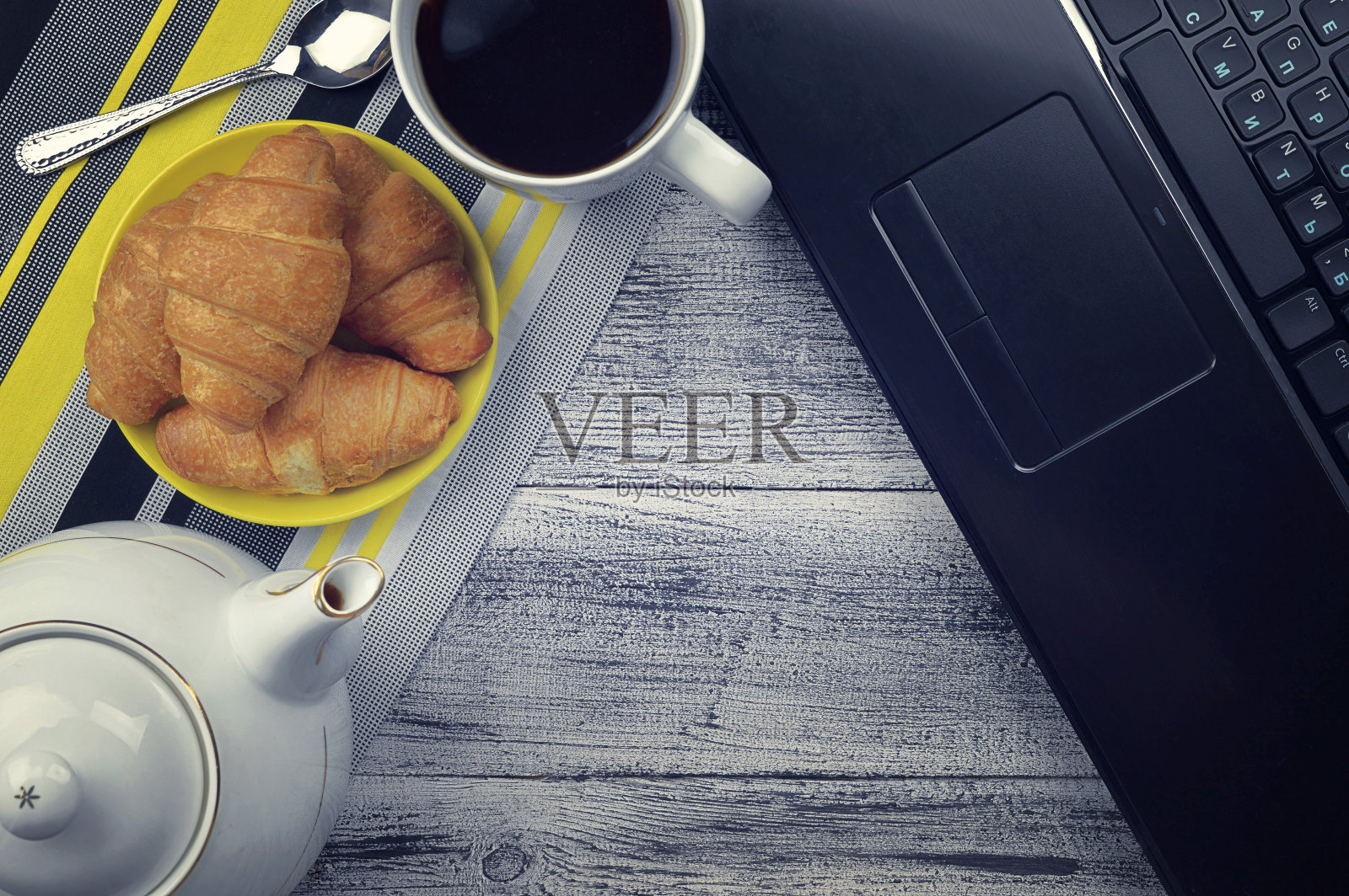 舒适和室内概念-笔记本电脑，一杯茶和羊角面包在一个深色的木制背景。平面布局，俯视图。照片摄影图片