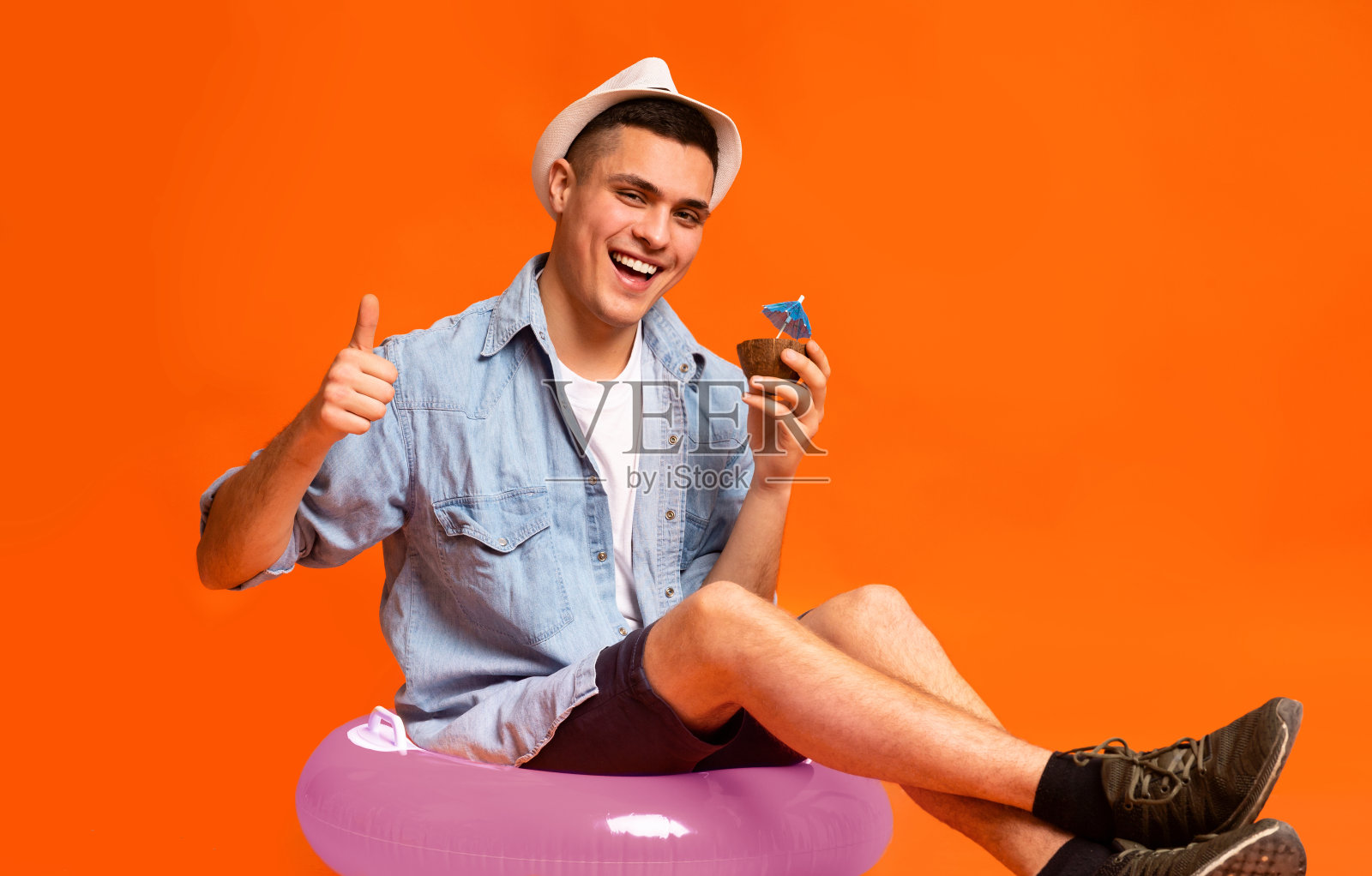 快乐的游客坐在粉红色的橡胶圈上，喝着鸡尾酒照片摄影图片