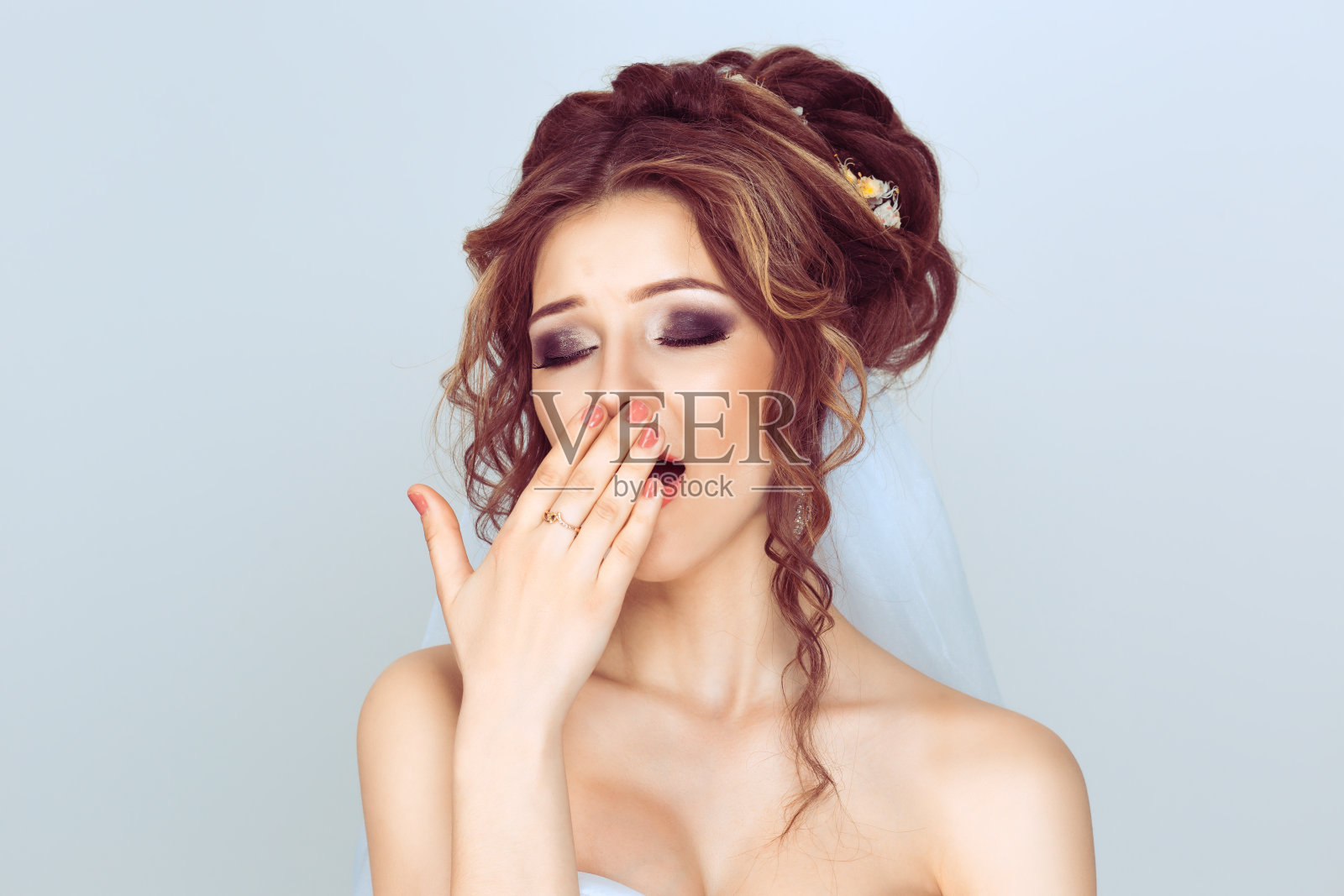 我想睡觉。时尚女学生新娘在影棚里摆姿势，婚礼后疲惫无聊，浅蓝色背景照片摄影图片