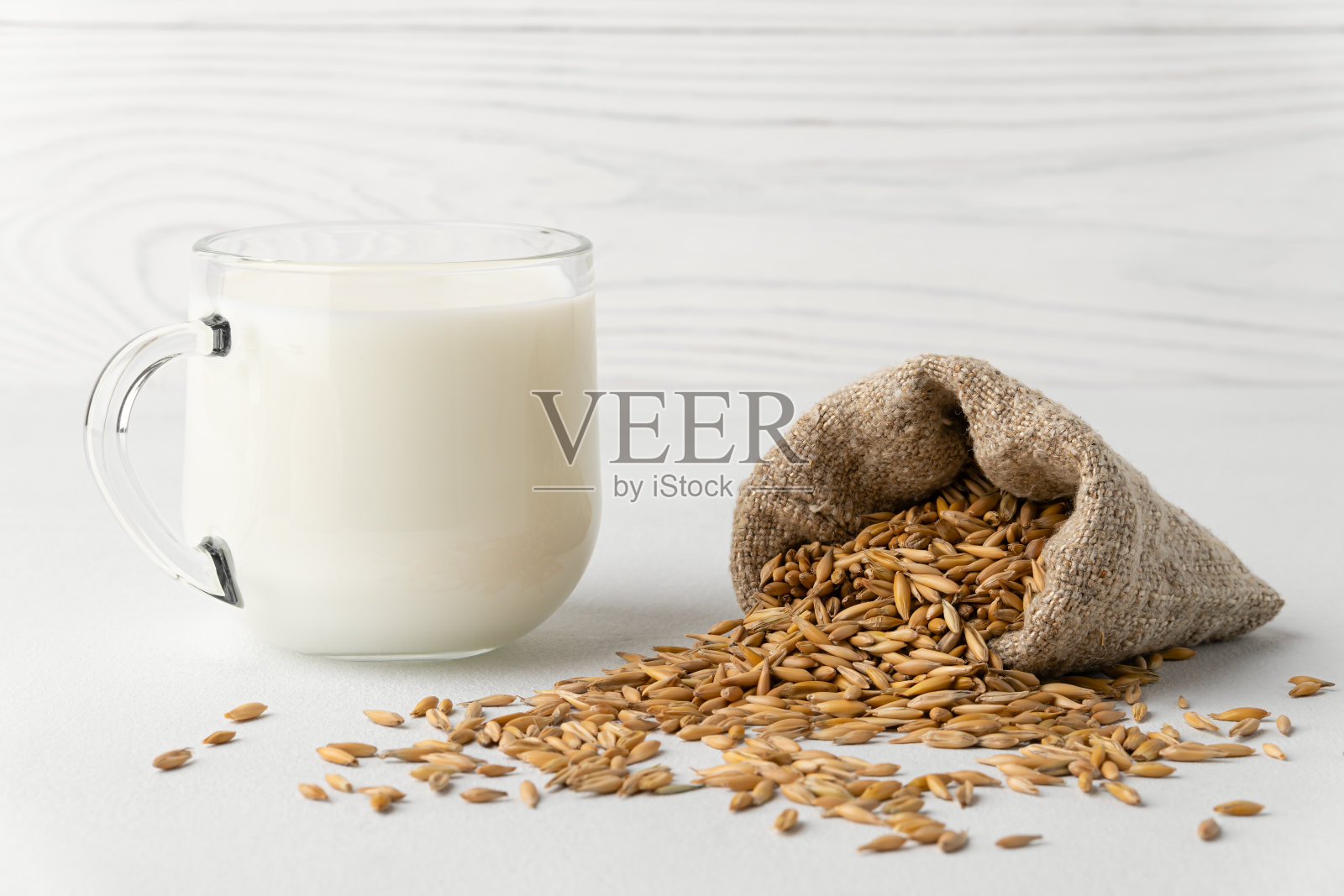 杯子里的燕麦牛奶和白色背景的小袋子里的谷物。照片摄影图片