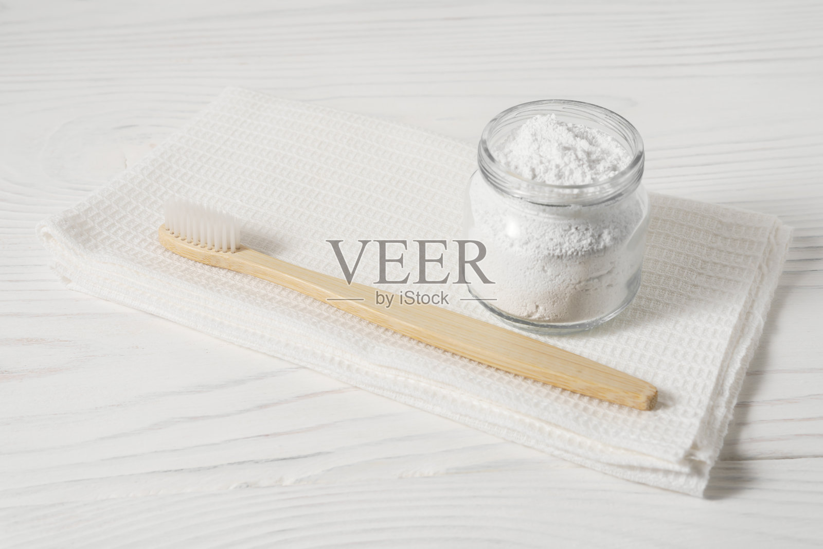 竹牙刷与白色的纺织品毛巾和粉末清洁牙齿的碗在一个轻木制的背景。照片摄影图片