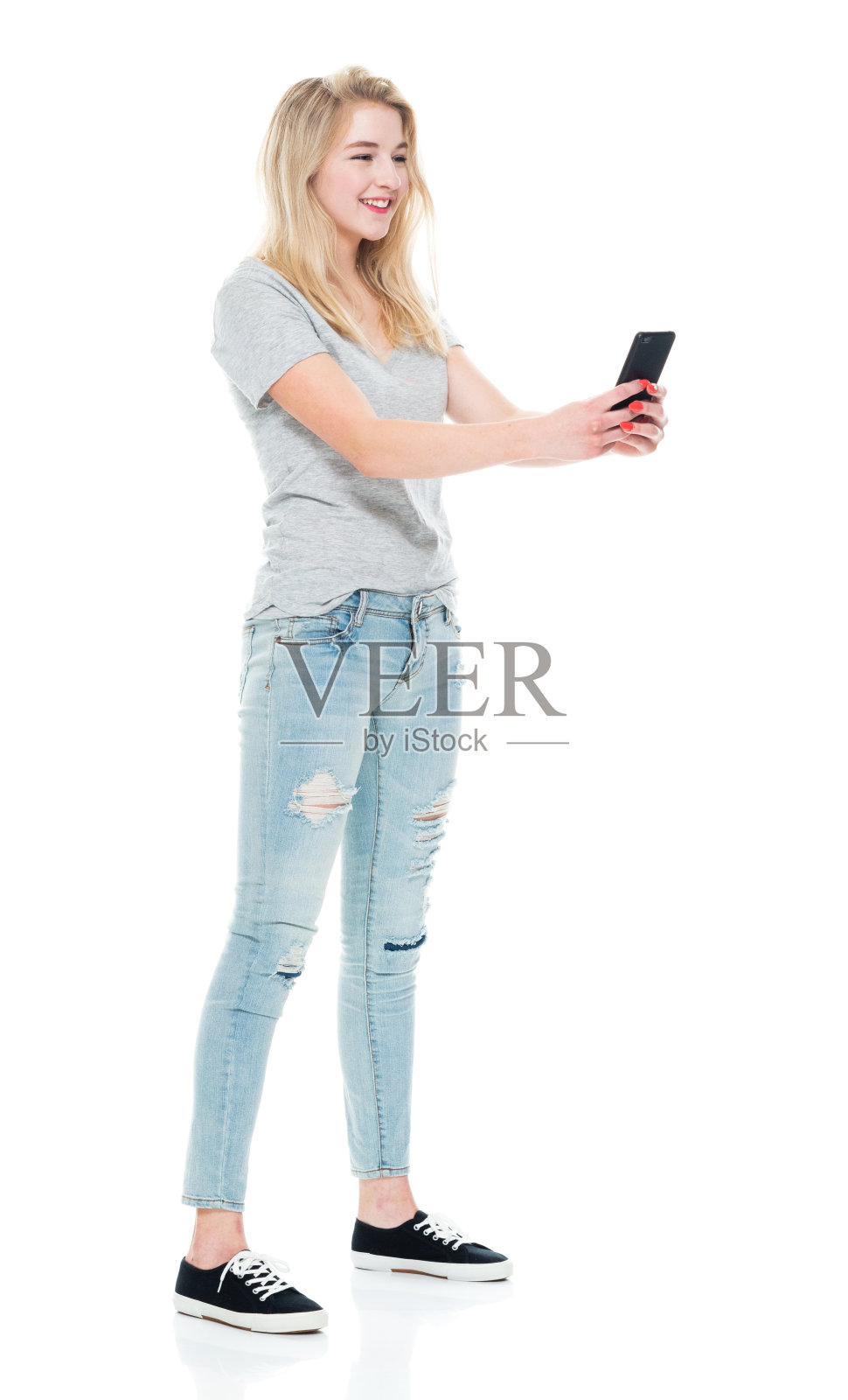 Z世代青少年女孩身穿牛仔裤站在白色背景前使用手机照片摄影图片