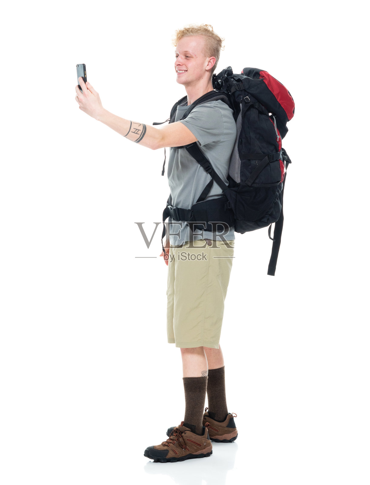 白人年轻男性穿着t恤，拿着包，用智能手机在白色背景前徒步旅行照片摄影图片