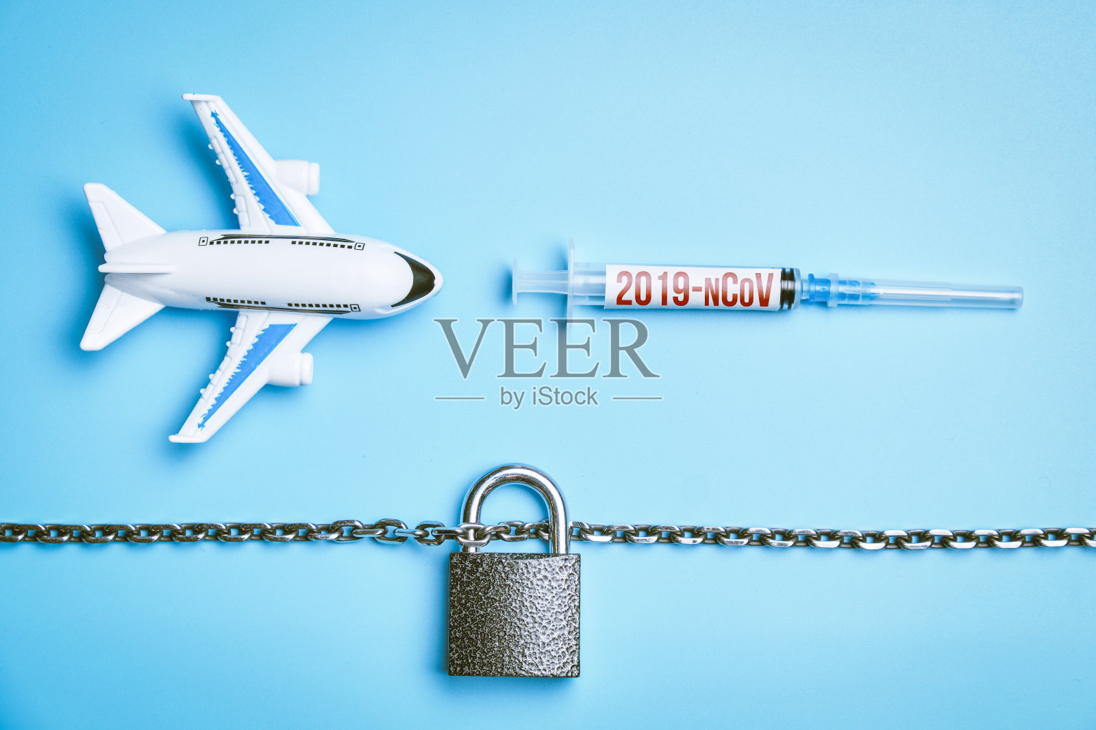 一架飞机旁边有一个刻着2019-ncov病毒的注射器，旁边是蓝色背景上的锁和链条。概念与禁飞保护。照片摄影图片