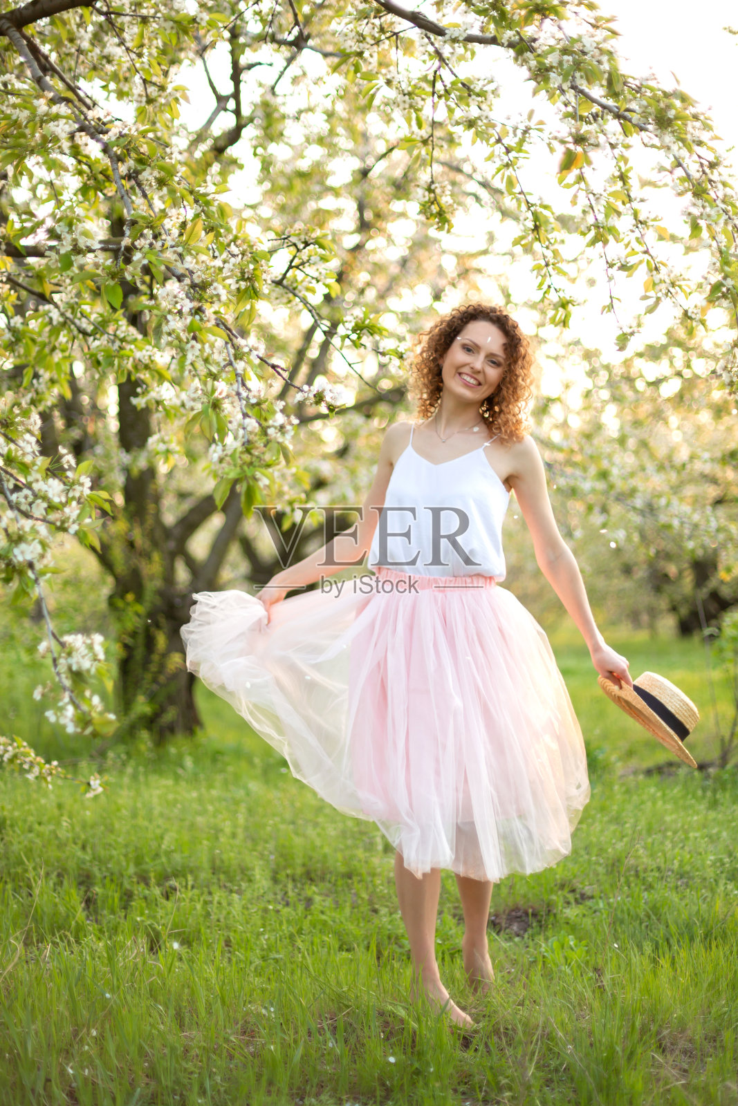 年轻卷发女子走在绿色花园中，充满浪漫气息照片摄影图片