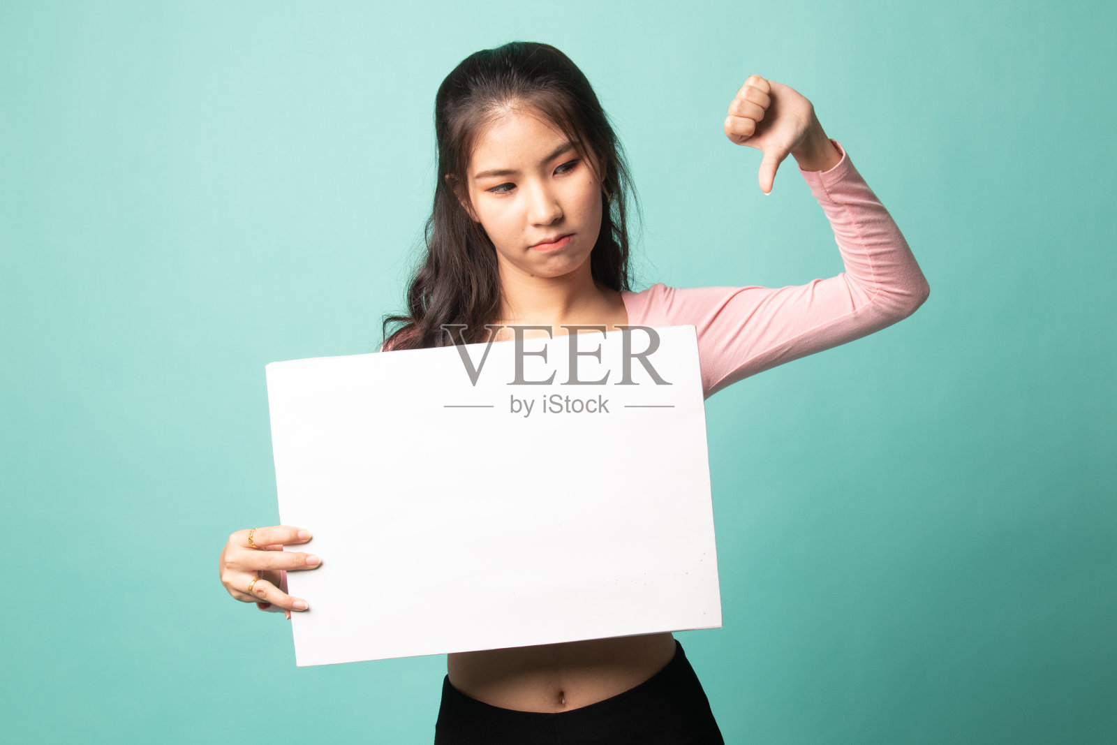 年轻的亚洲女人用白色的空白手势表示拇指向下。照片摄影图片