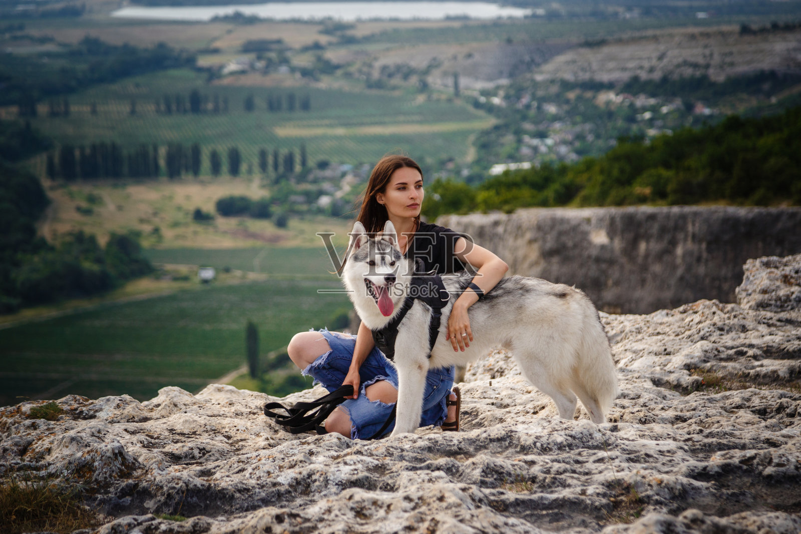 日落时分，美丽的女孩和一只灰白相间的哈士奇狗在山上玩耍。照片摄影图片