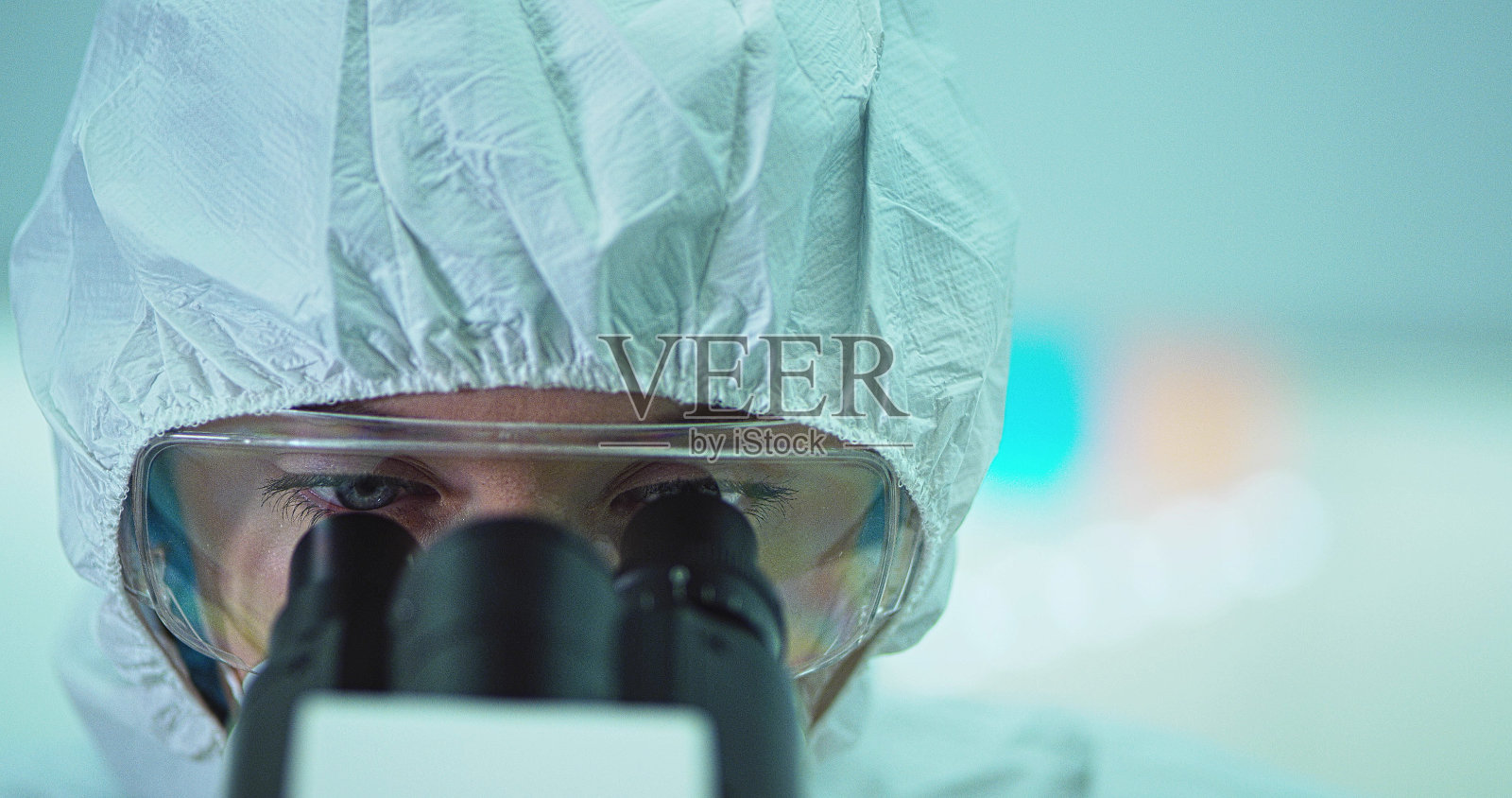 戴着医用帽子和眼镜，通过显微镜观察的女子照片摄影图片