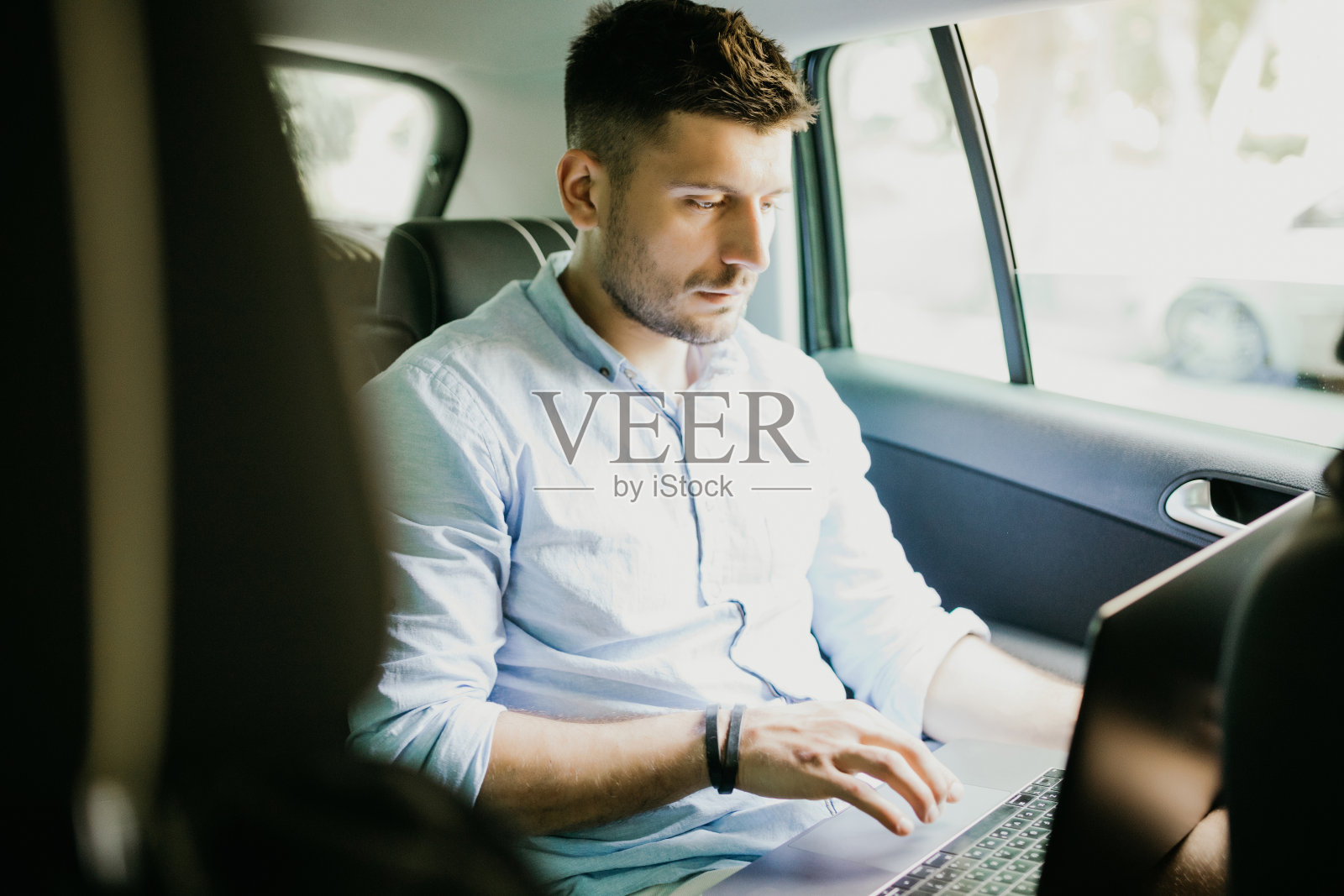 男子在汽车后座用笔记本电脑工作的肖像照片摄影图片