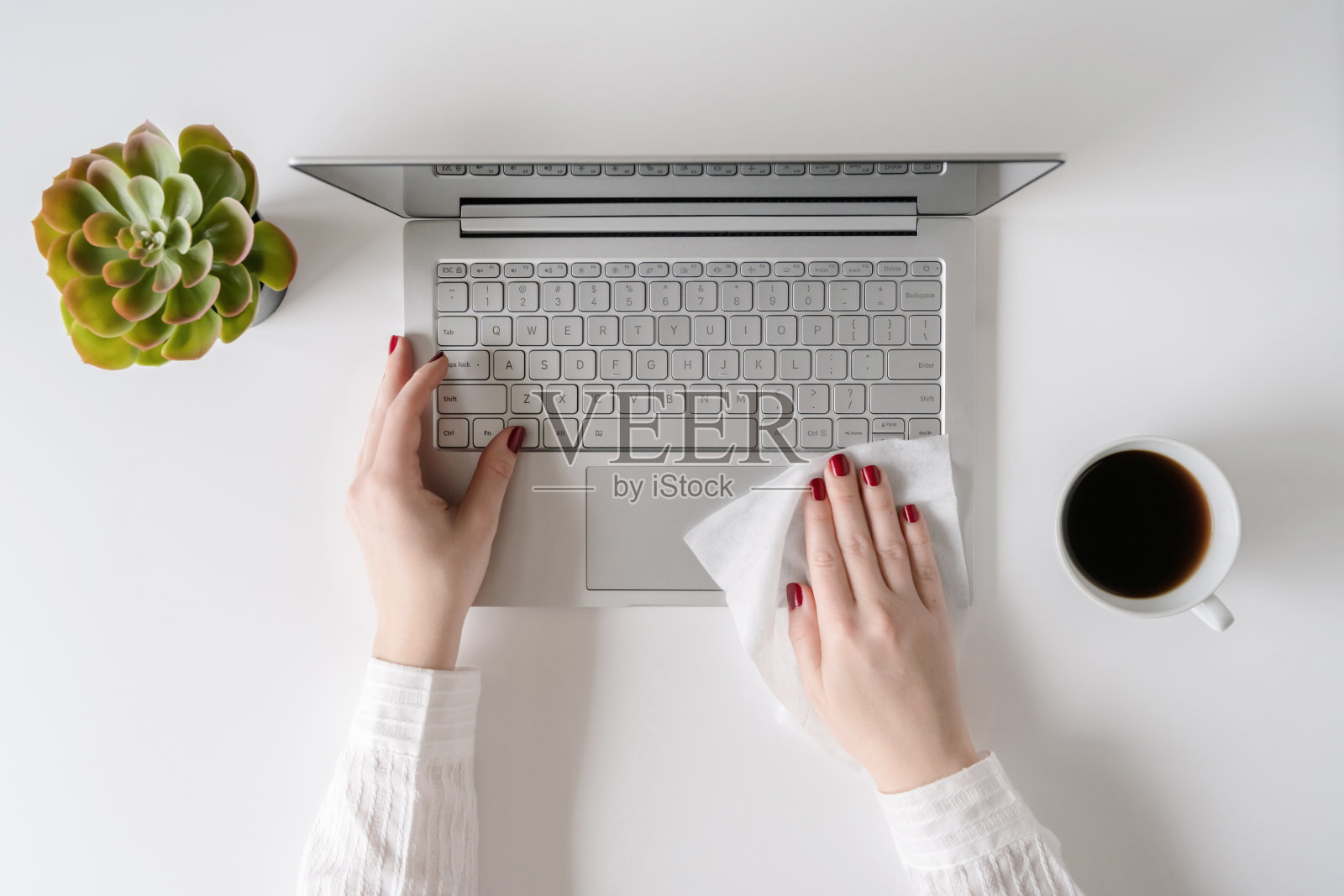 一名女工在开始工作前，用防病毒湿巾擦拭笔记本电脑和办公桌，以保护自己免受细菌和病毒的伤害。照片摄影图片