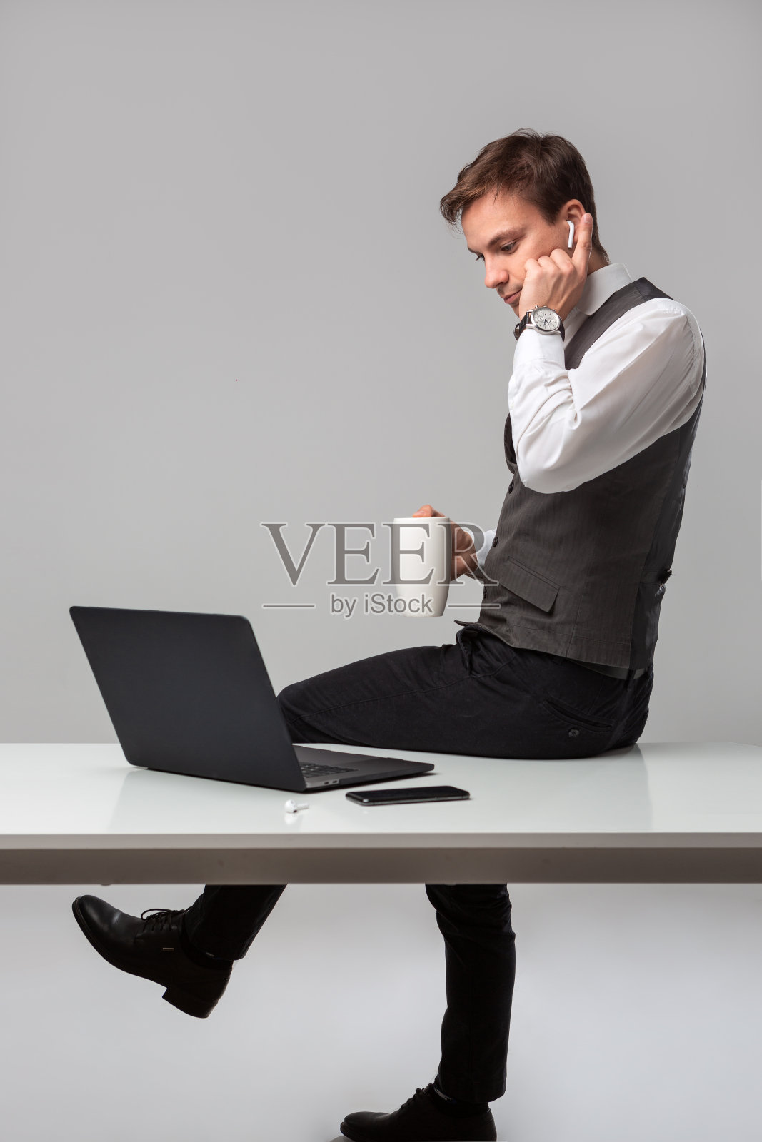 男人坐在放有笔记本电脑和智能手机的白色桌子旁喝咖啡照片摄影图片