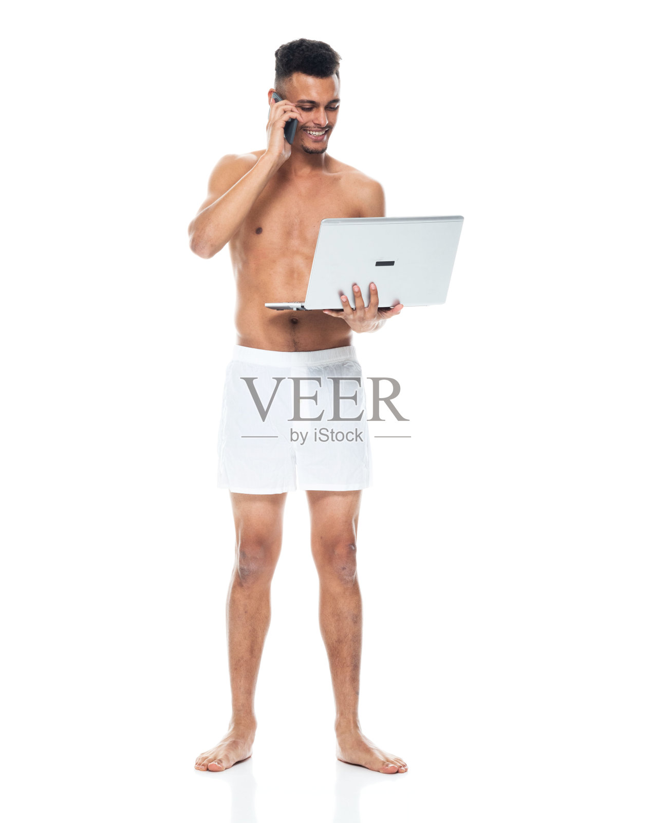 非裔美国青年男性穿着内衣，使用笔记本电脑站在白色背景前照片摄影图片