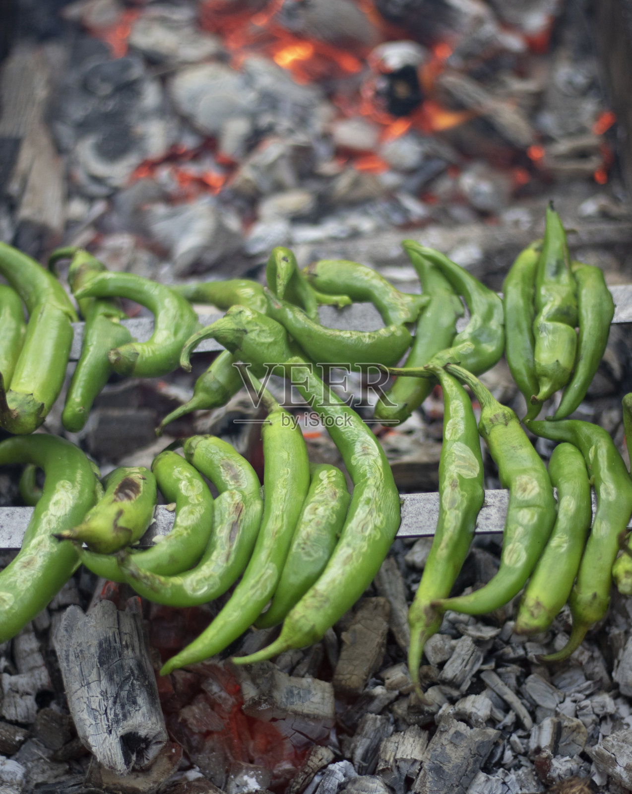 青椒和瓶子放在烤架上。在它下面的木炭里烤着的余烬很热。特写镜头。照片摄影图片