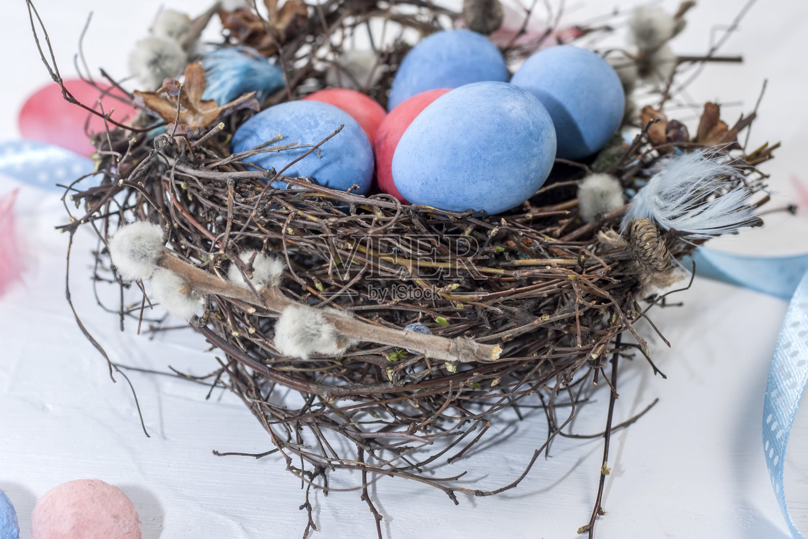在白色纹理的背景上，用柳条、羽毛和丝带装饰的小树枝巢中绘制复活节鹌鹑蛋照片摄影图片