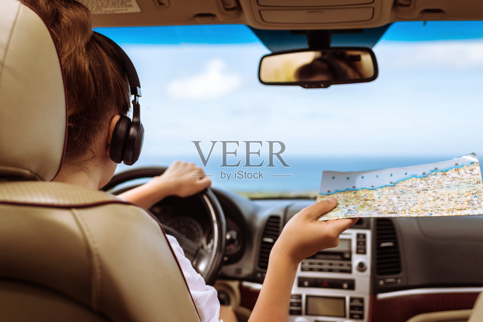 女司机戴着耳机开车并查看地图。在热带海滩背景下享受汽车旅行照片摄影图片