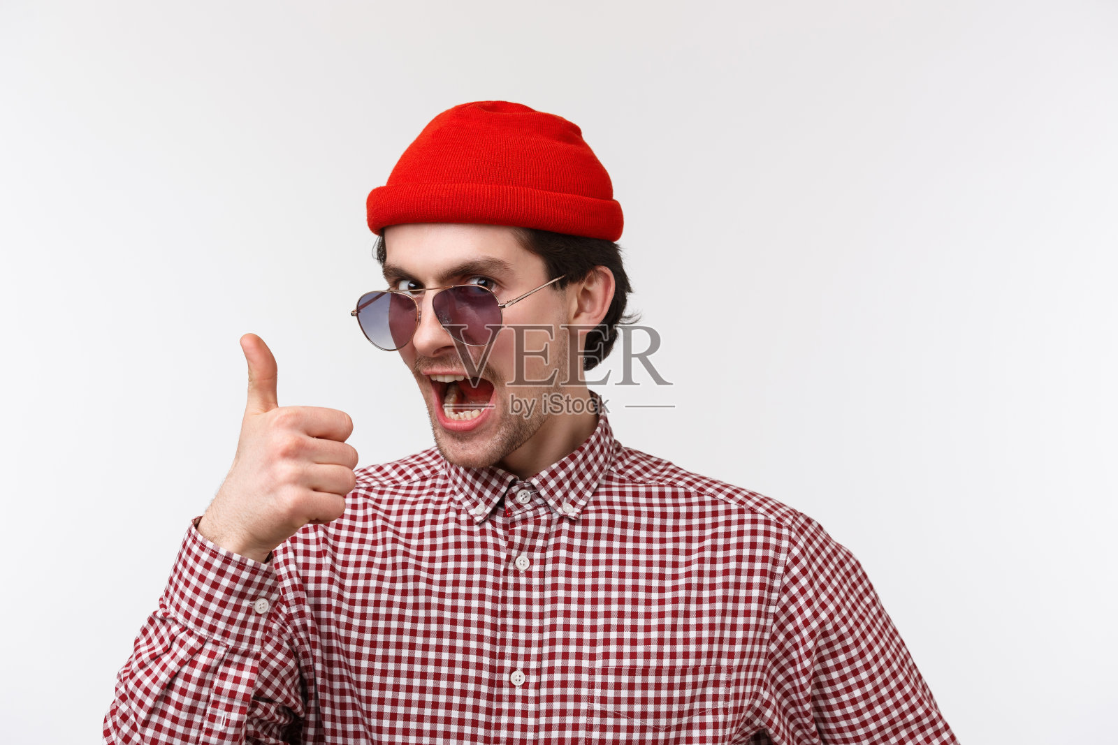 兴奋英俊有趣的小胡子年轻人，戴太阳镜和红色潮人无檐帽，翘起大拇指，看着相机鼓励购买产品，满意赞扬朋友的工作照片摄影图片