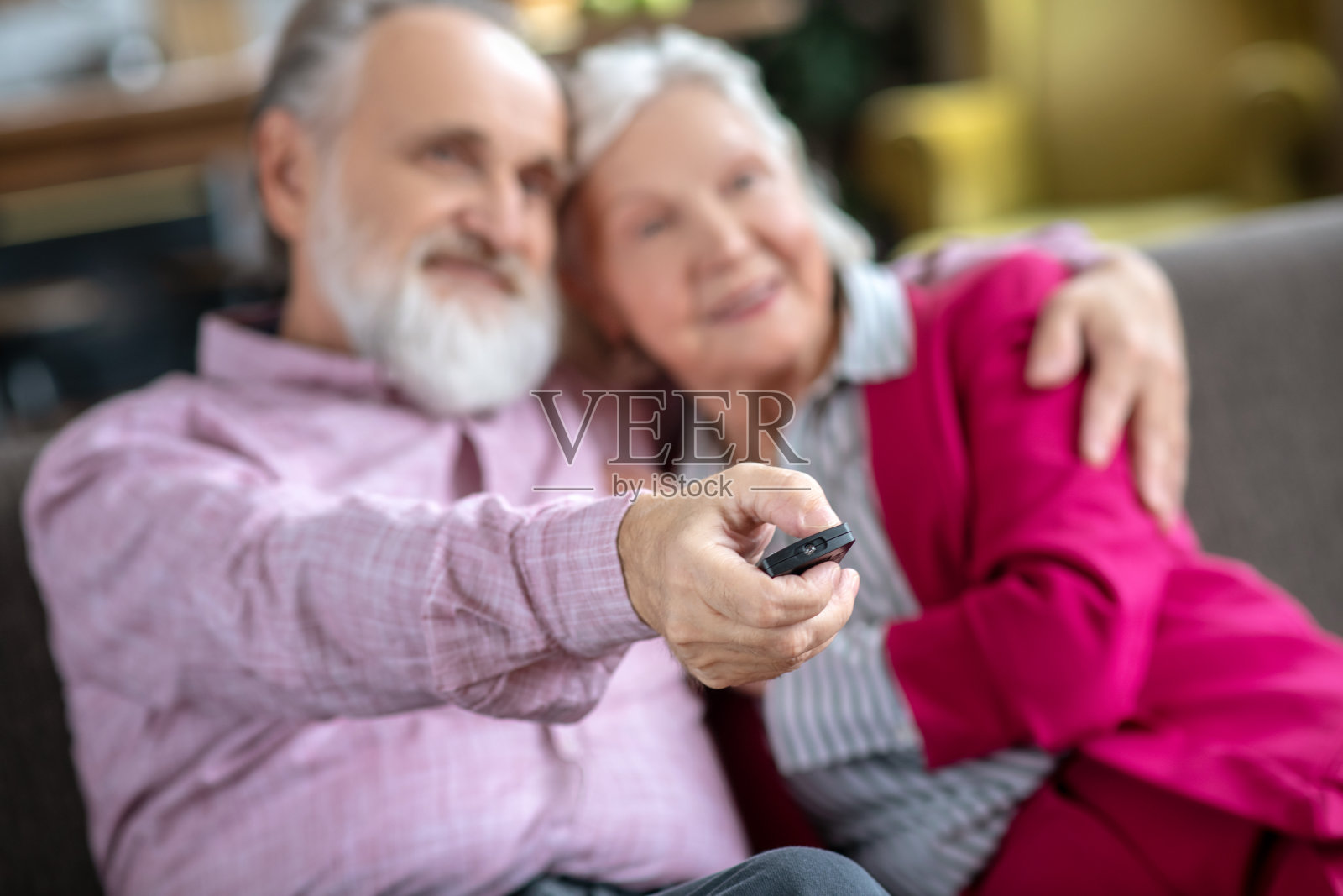 一个穿着粉红色衬衫的男人拥抱着他的妻子，同时打开电视照片摄影图片