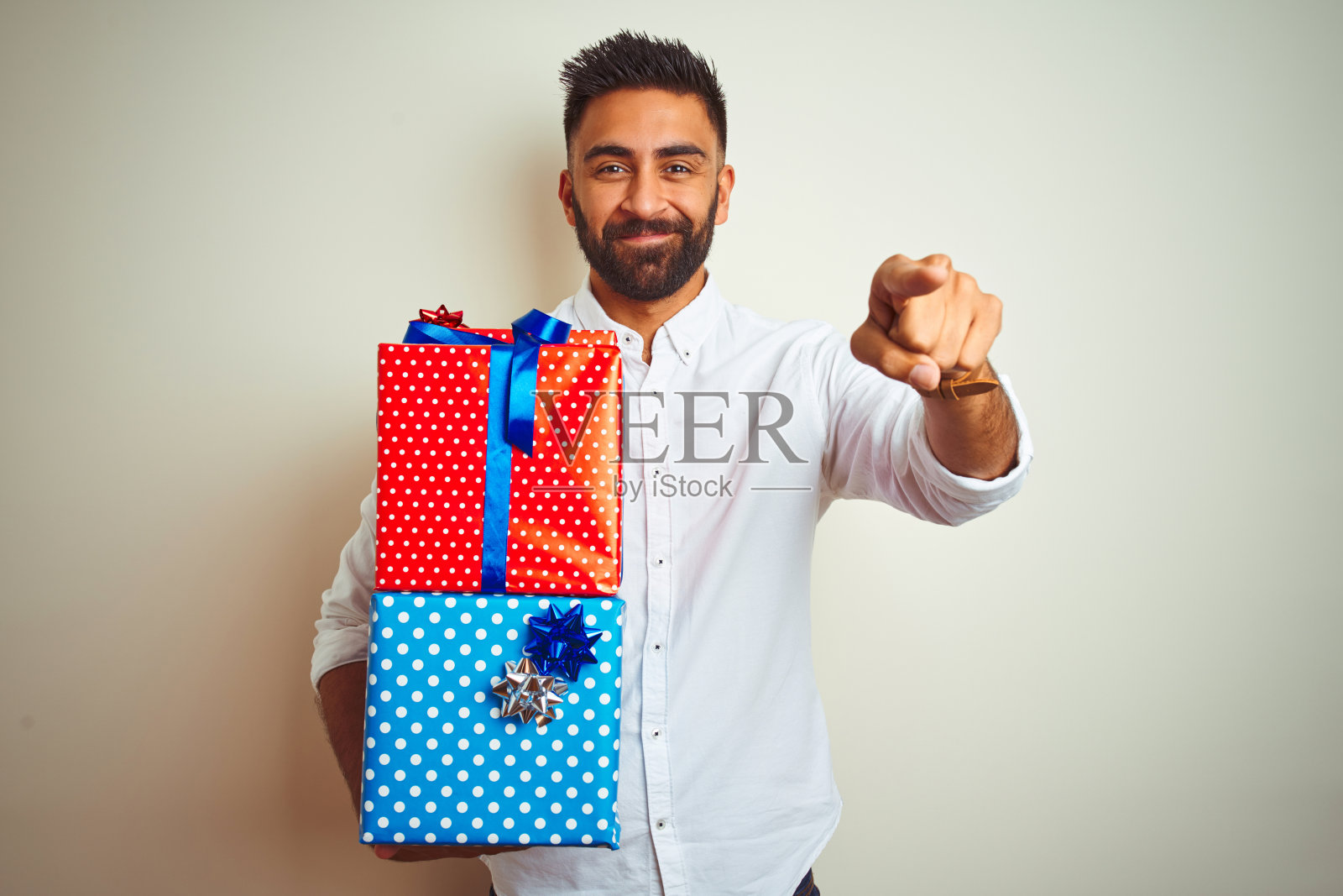 拿着生日礼物，站在孤立的白色背景前，用手指着相机和你的年轻阿拉伯印度裔西班牙裔男子，手势，积极和自信的手势照片摄影图片