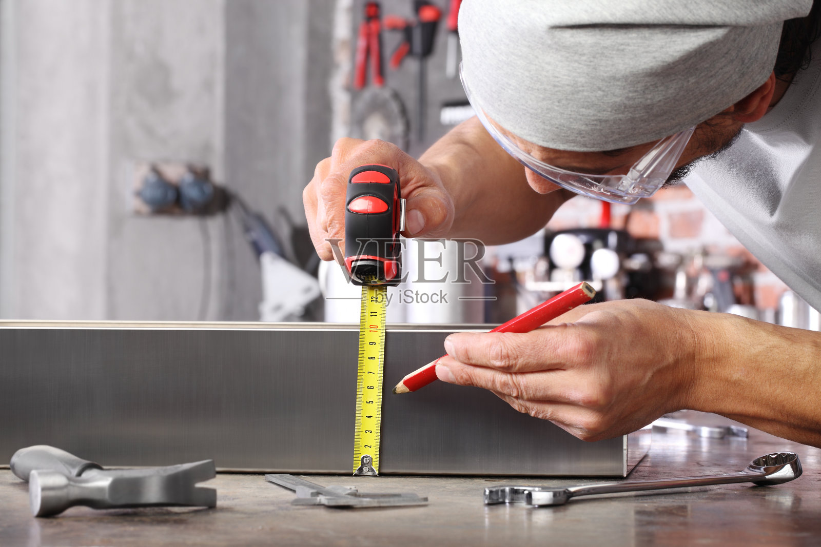 工人在家庭车间车库用卷尺和铅笔测量金属，在工作台上用扳手和锤子，diy和工艺概念照片摄影图片