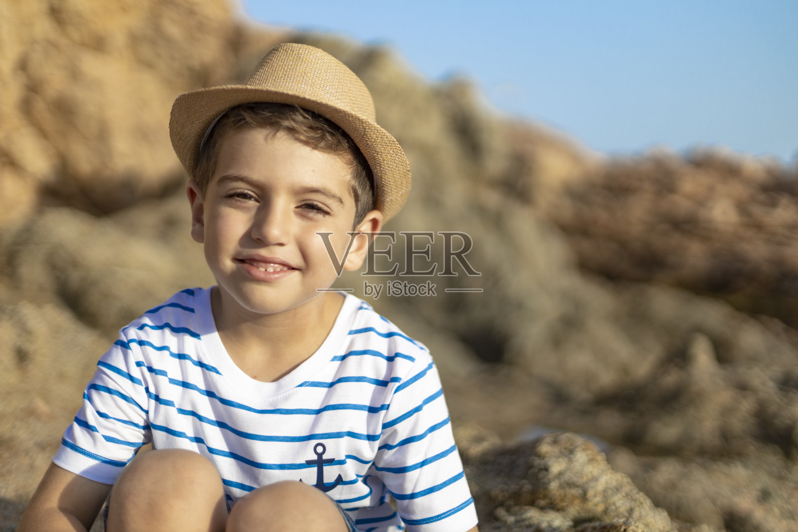 一个可爱的孩子坐在海边的岩石上的肖像照片摄影图片