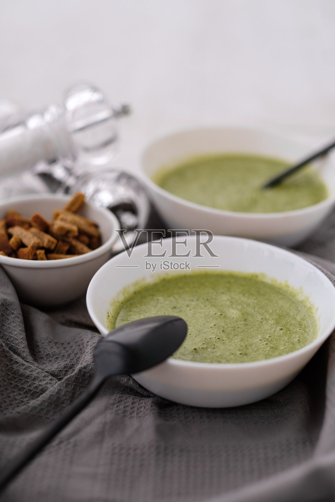 春季排毒花椰菜绿奶油汤在白色的盘子，碗与饼干和时尚的黑色餐具在灰色的背景。照片摄影图片