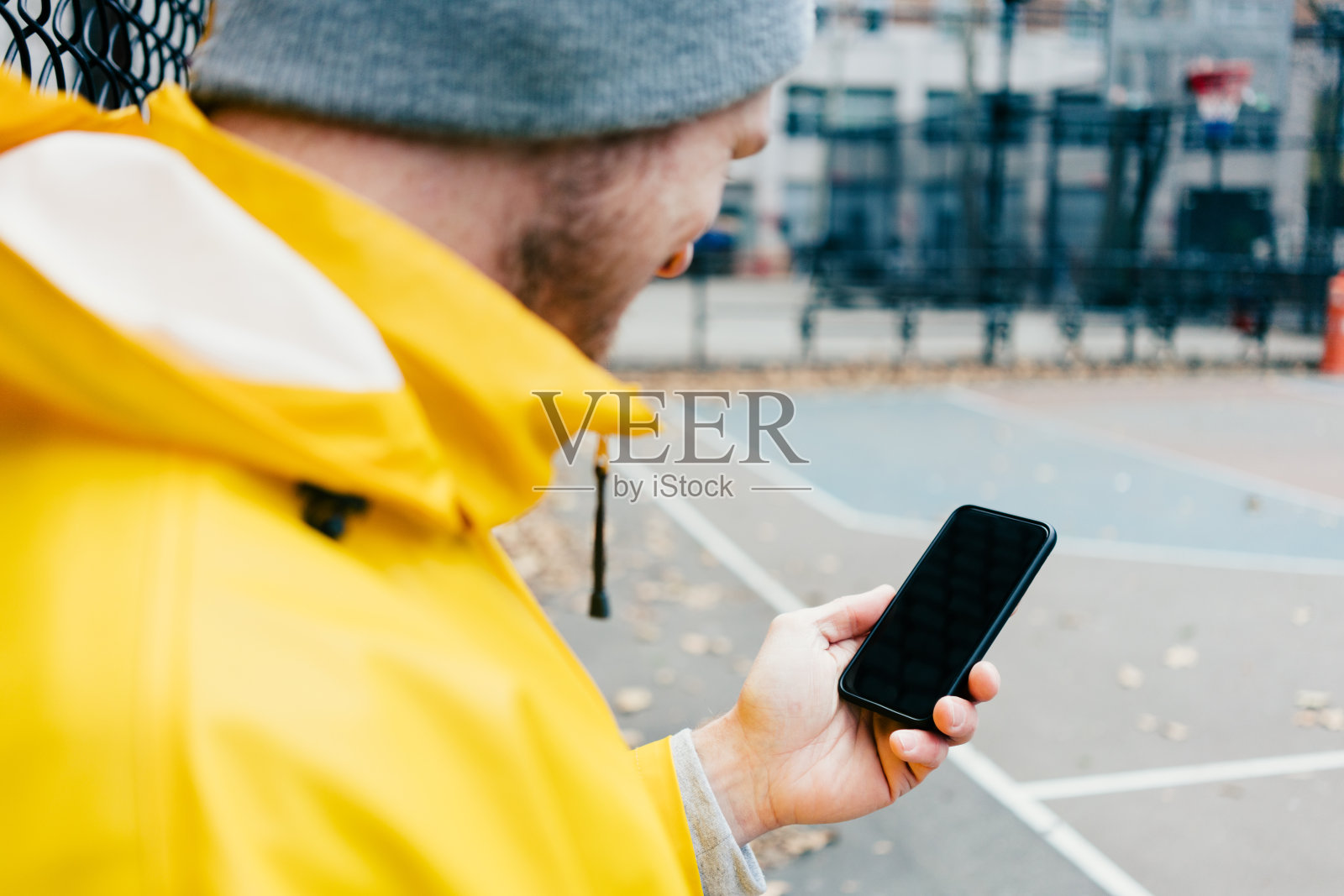 一个穿着黄色雨衣的年轻人手里拿着手机站在操场上的街道上照片摄影图片