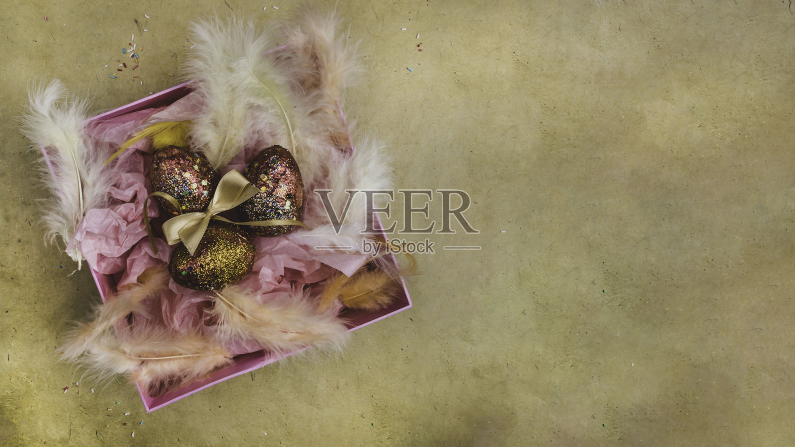 复活节彩蛋装在带有羽毛的粉色礼品盒里，作为复活节的装饰。巢与金红色的蛋在节日背景贺卡。复活节快乐。照片摄影图片