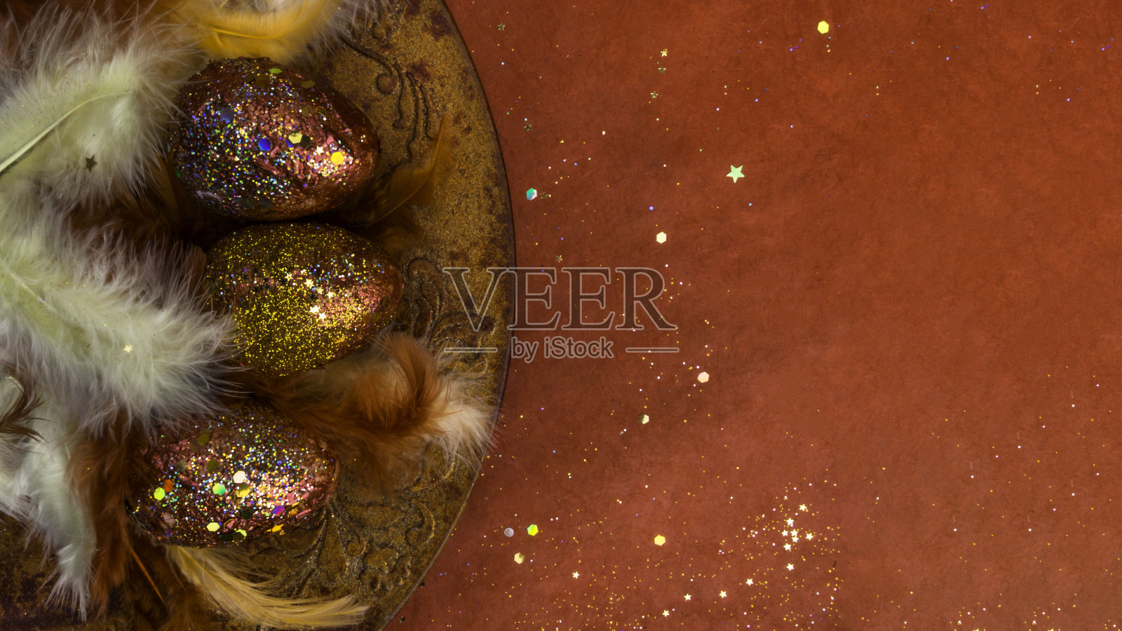 顶视图的节日贺卡与金红色的鸡蛋，羽毛与节日闪闪发光的五彩纸屑在红色的背景。复活节快乐概念照片摄影图片